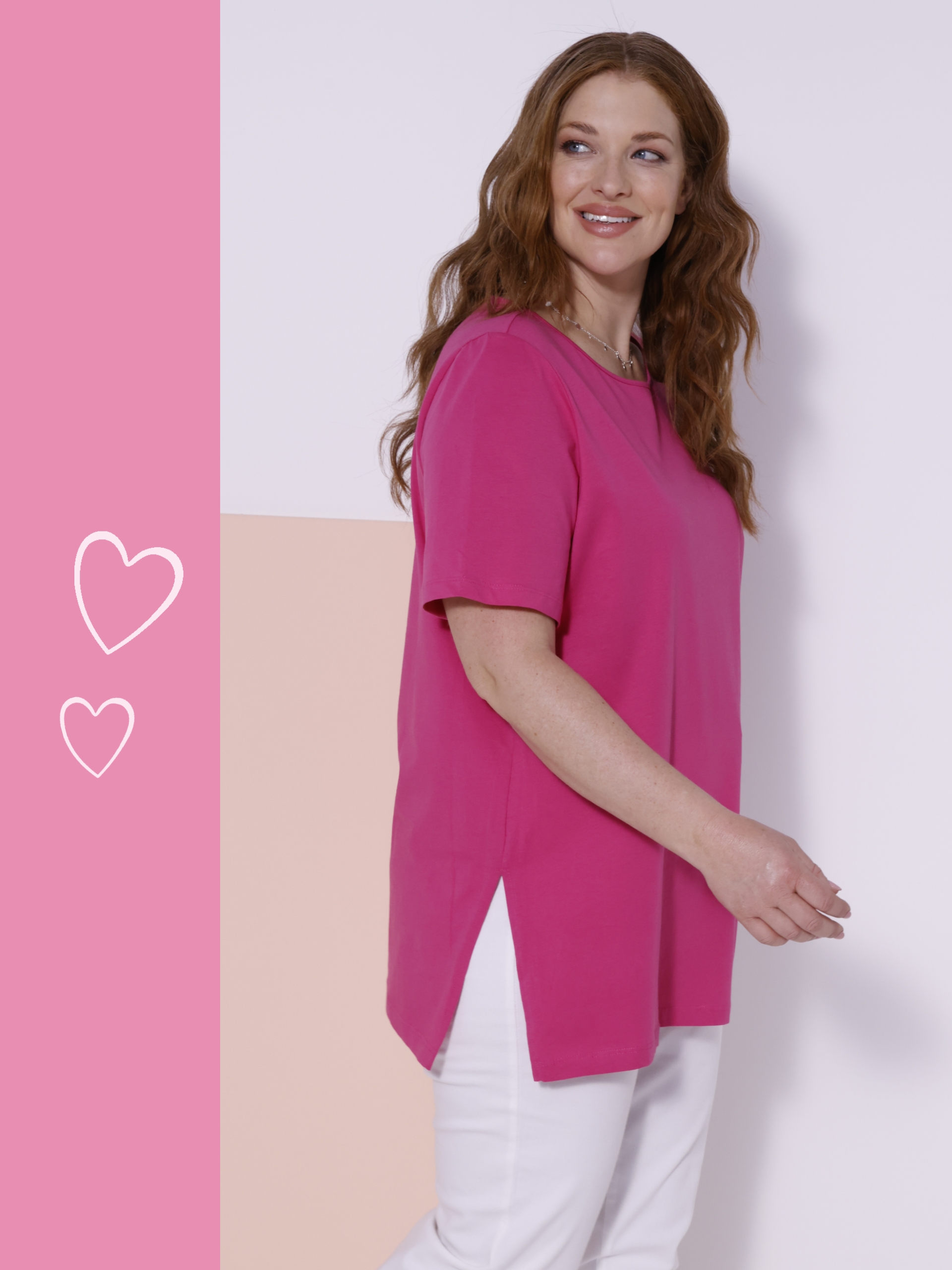 Ein Model steht seitlich vor einer zweifarbigen Wand, trägt ein pinkes T-Shirt mit kurzen Ärmeln und weiße Hosen.