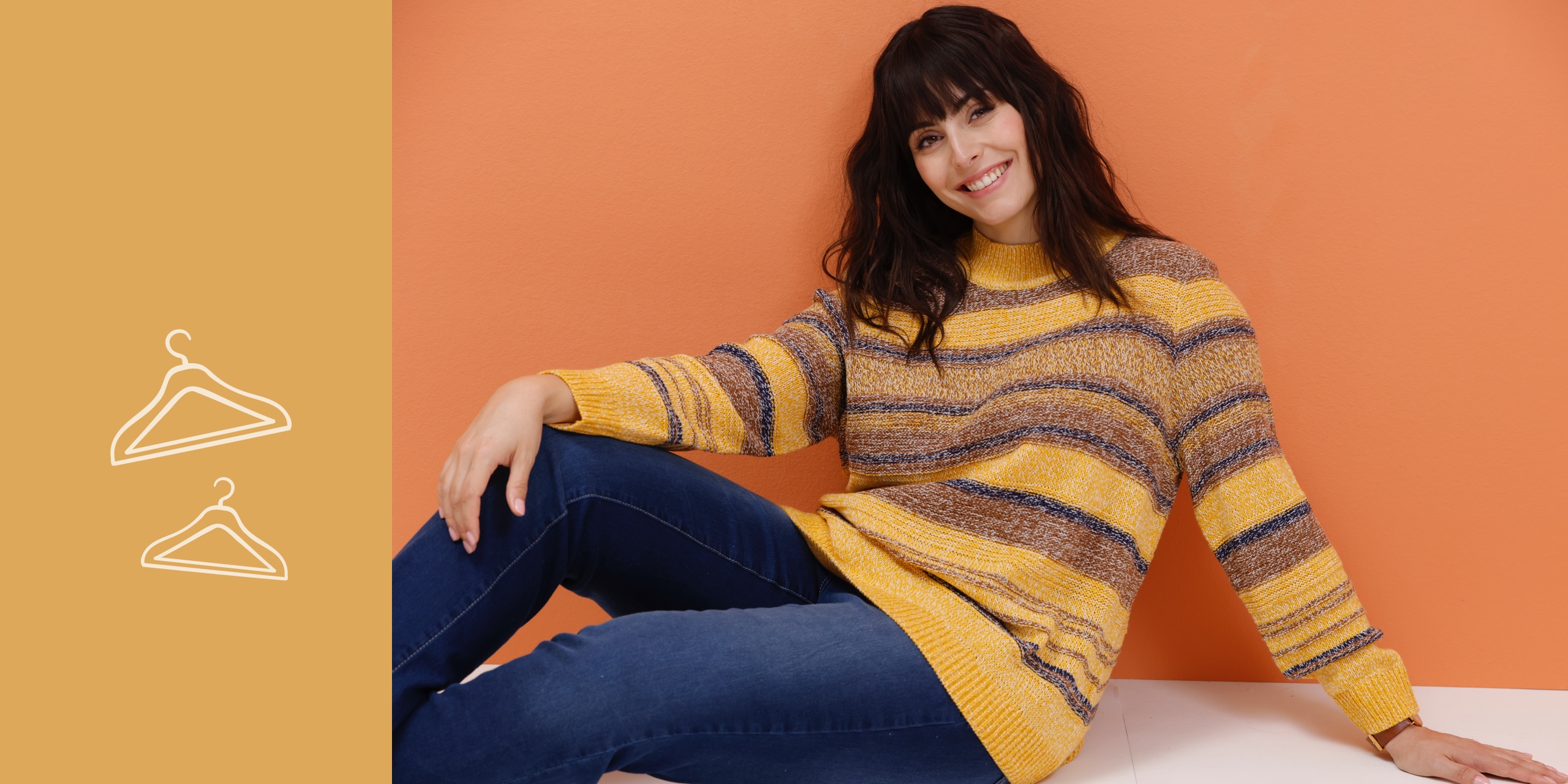 Ein Model liegt auf dem Bauch in einem blauen Pullover mit Muster und Jeans, vor einem orangefarbenen Hintergrund.