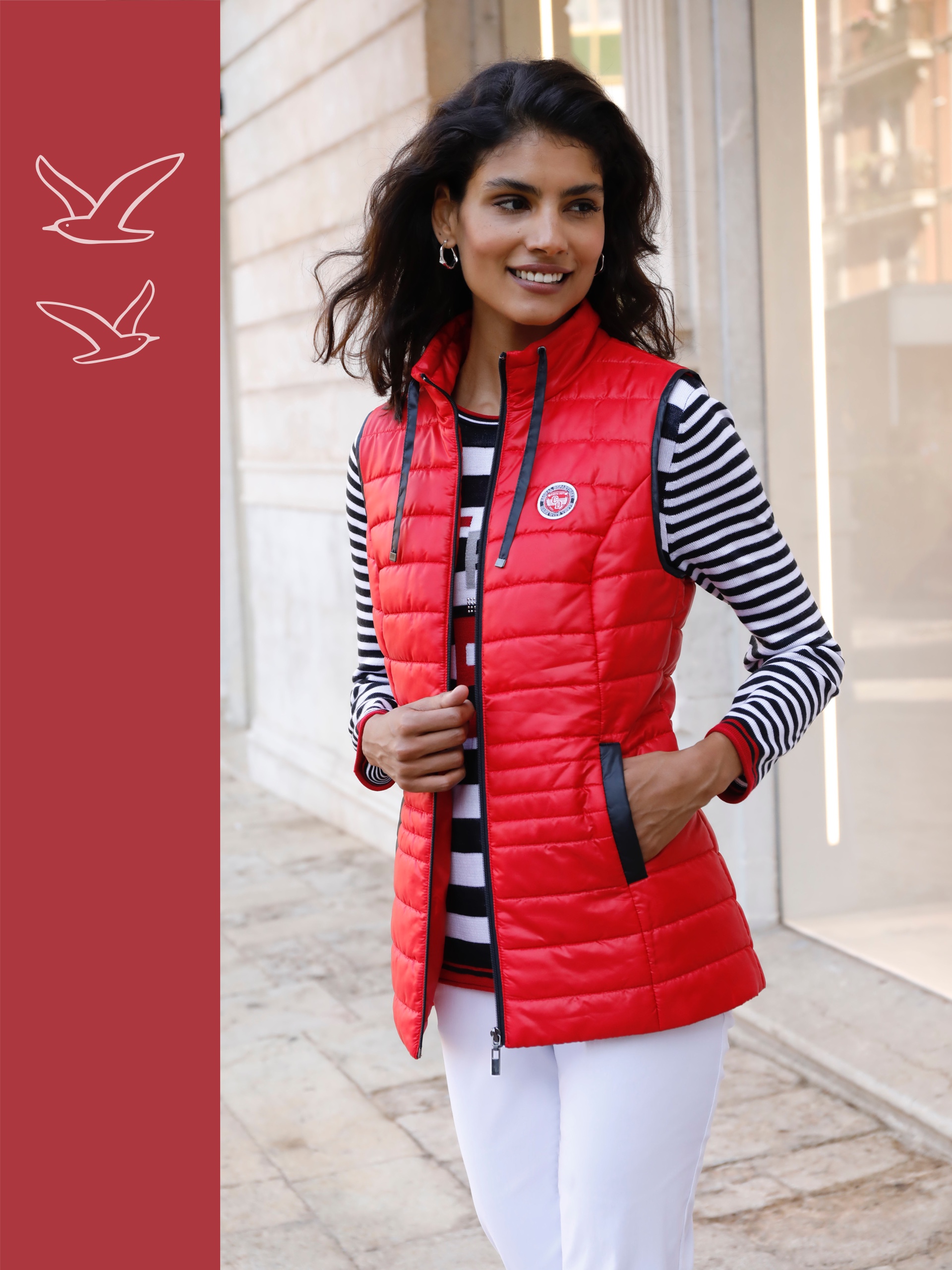 Ein Model trägt eine rote Steppweste über einem gestreiften Shirt und weißen Hosen. Der Hintergrund zeigt eine städtische Umgebung.