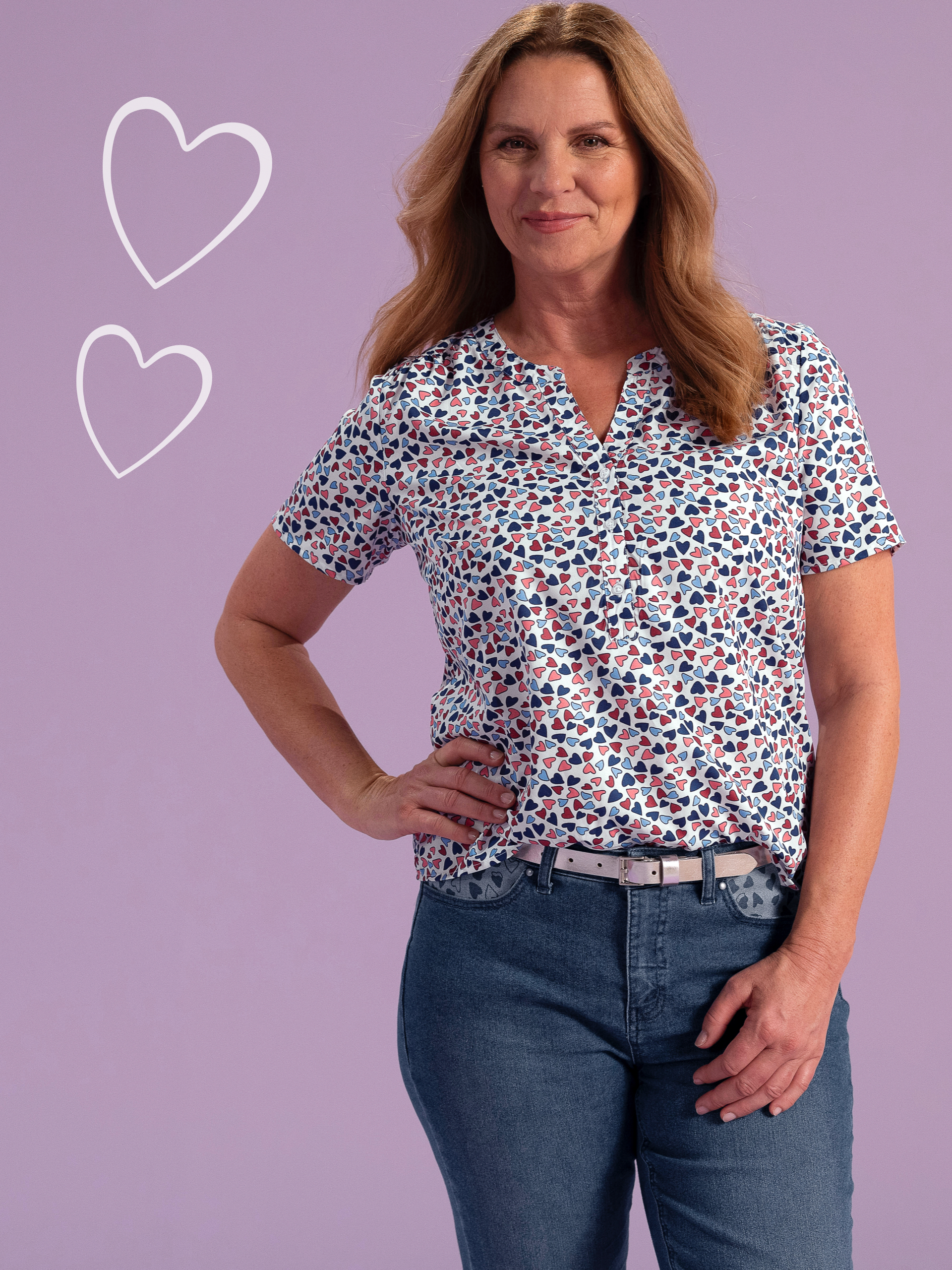 Frau trägt eine kurzärmelige Bluse mit buntem Herzmuster und dazu eine blaue Jeans, lila Hintergrund mit gezeichneten Herzen.