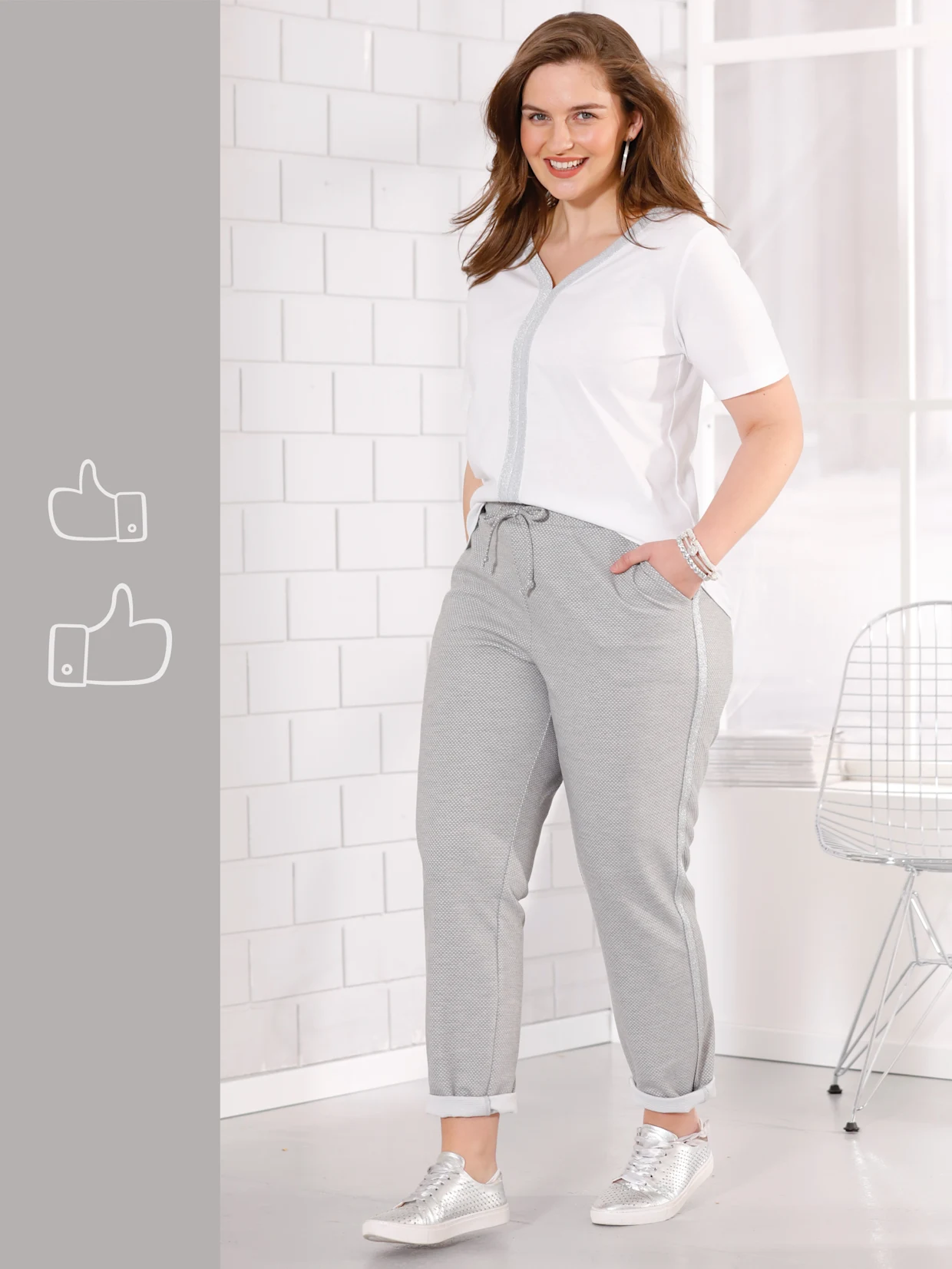 Ein Model trägt ein weißes T-Shirt und graue Jogginghosen mit Sneakers, während es vor einer weißen Ziegelwand steht.