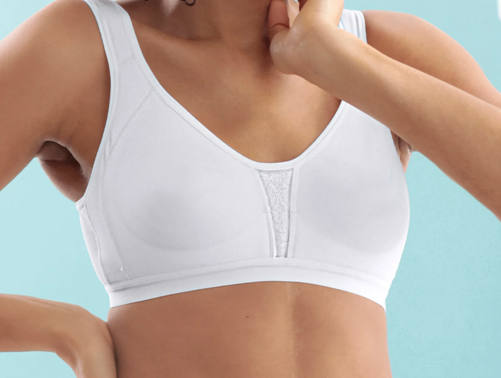 Žena oblečená v bílém pohodlném podprsence bez kostic na modrém pozadí.