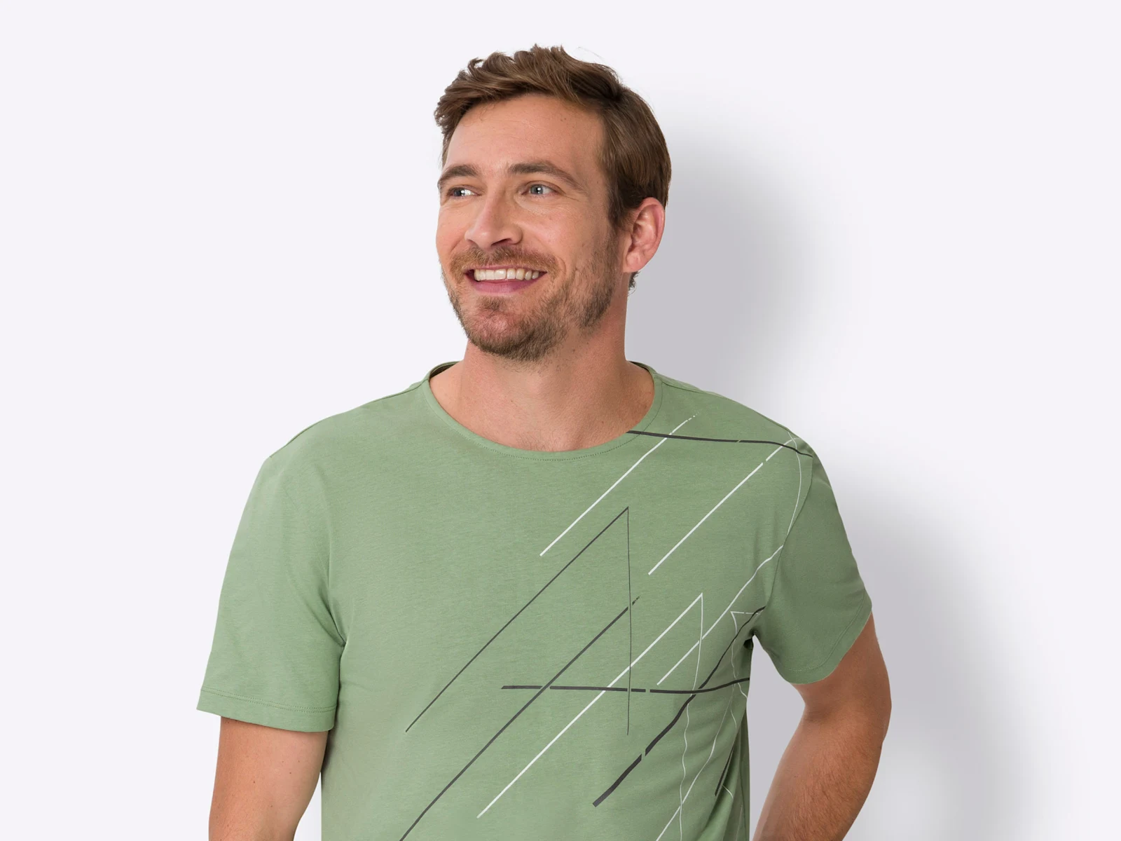 Een model met kort bruin haar draagt een groen T-shirt met zwart-wit lijnpatroon en lacht.