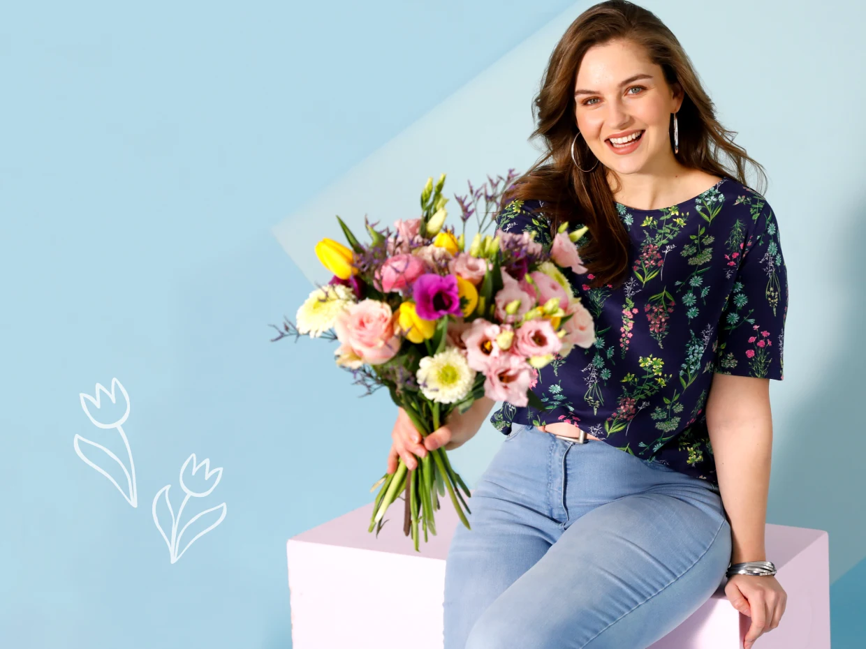 Frau mit Blumen-Shirt in grosse Groessen und Blumenstrauss in der Hand