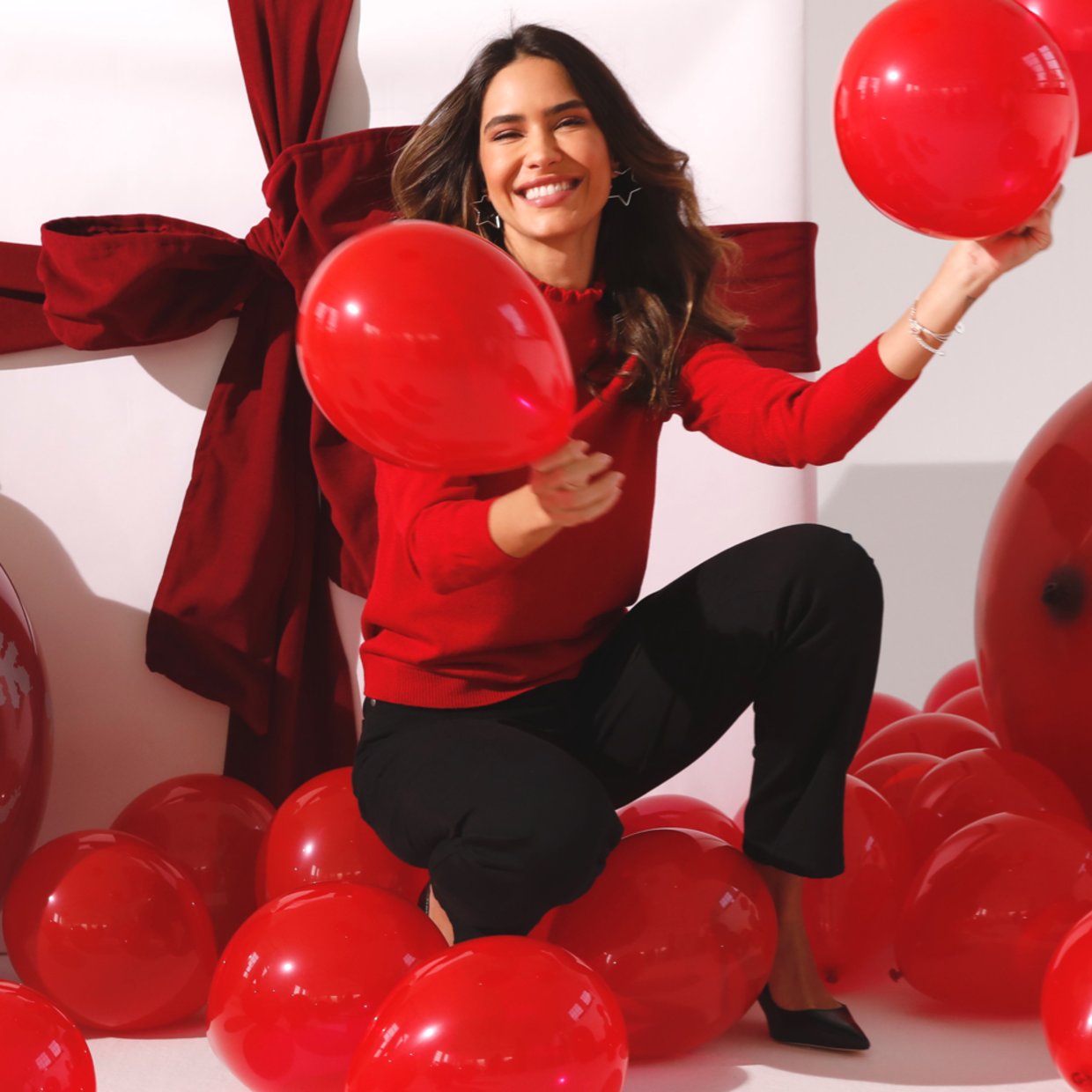 Frau mit rotem Oberteil vor Geschenkpaket mit roten Luftballons in der Hand