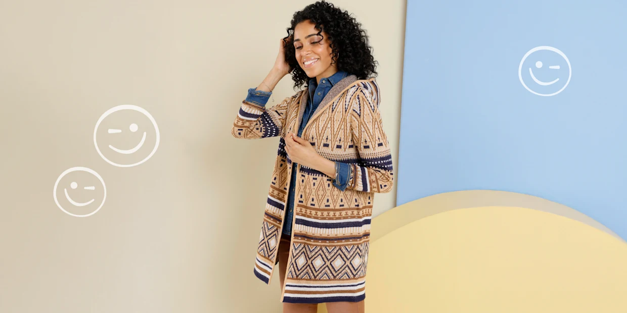 Ein Model trägt eine lange Strickjacke mit Kapuze und geometrischem Muster in Beige, Braun und Dunkelblau über einem Jeanshemd. Ein Model trägt eine lange Strickjacke mit Kapuze und geometrischem Muster in Beige, Braun und Dunkelblau über einem Jeanshemd.