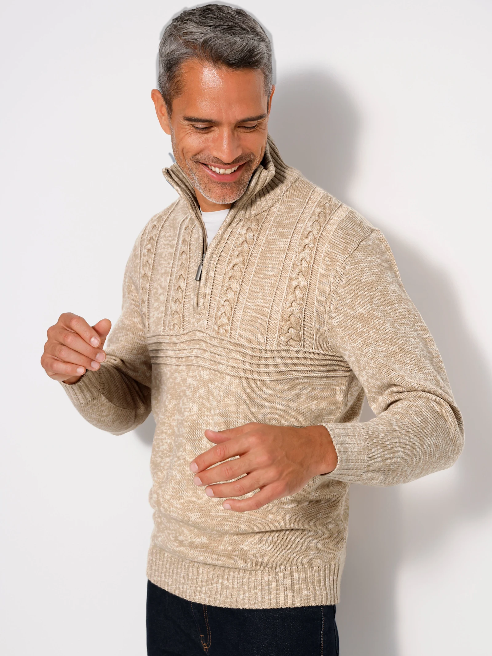 Een model draagt een beige gebreide trui met rits en kabelpatroon.