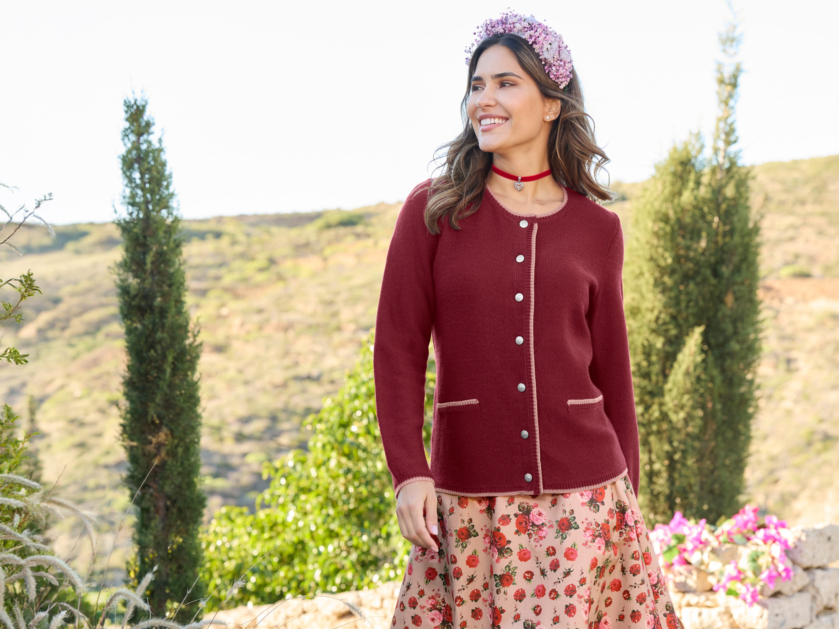 Ein Model trägt eine bordeauxrote Strickjacke und einen Rock mit Rosenmuster.