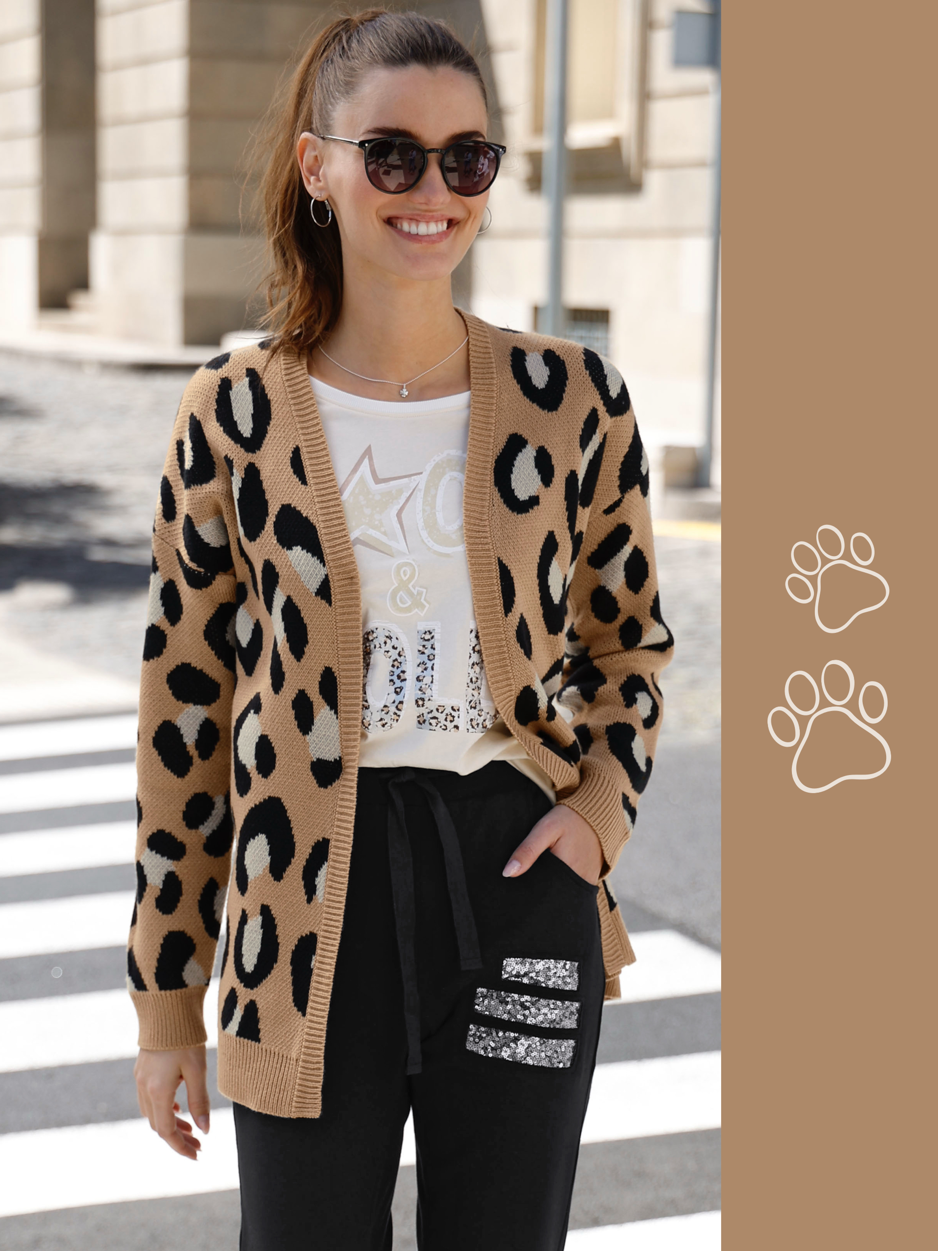 Model má na sebe béžový pletený sveter s leopardím vzorom, biele tričko s potlačou a čierne nohavice s flitrovými aplikáciami.