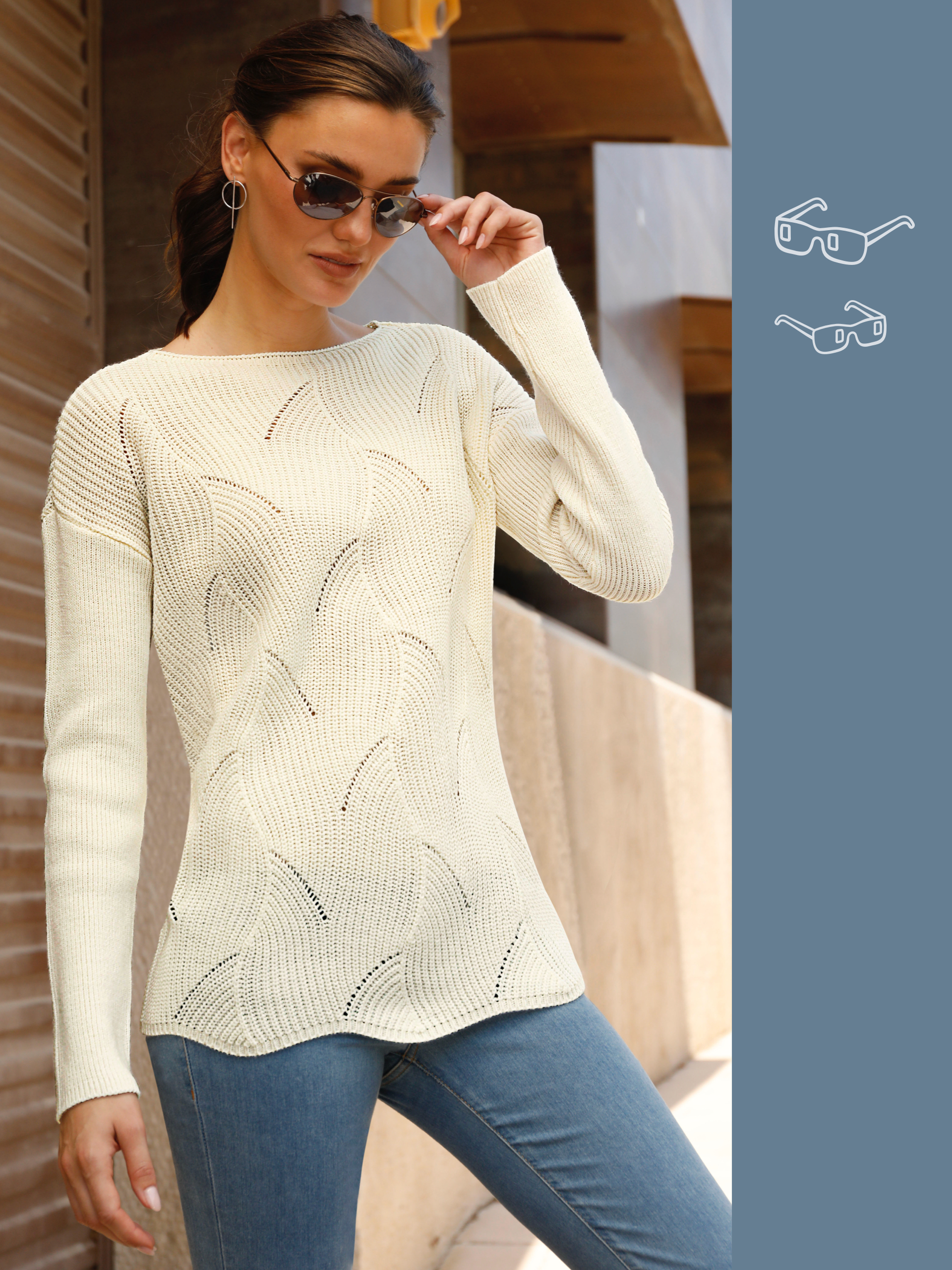 Ein Model trägt einen cremefarbenen, langärmligen Strickpullover mit feinem Muster und eine blaue Jeans.