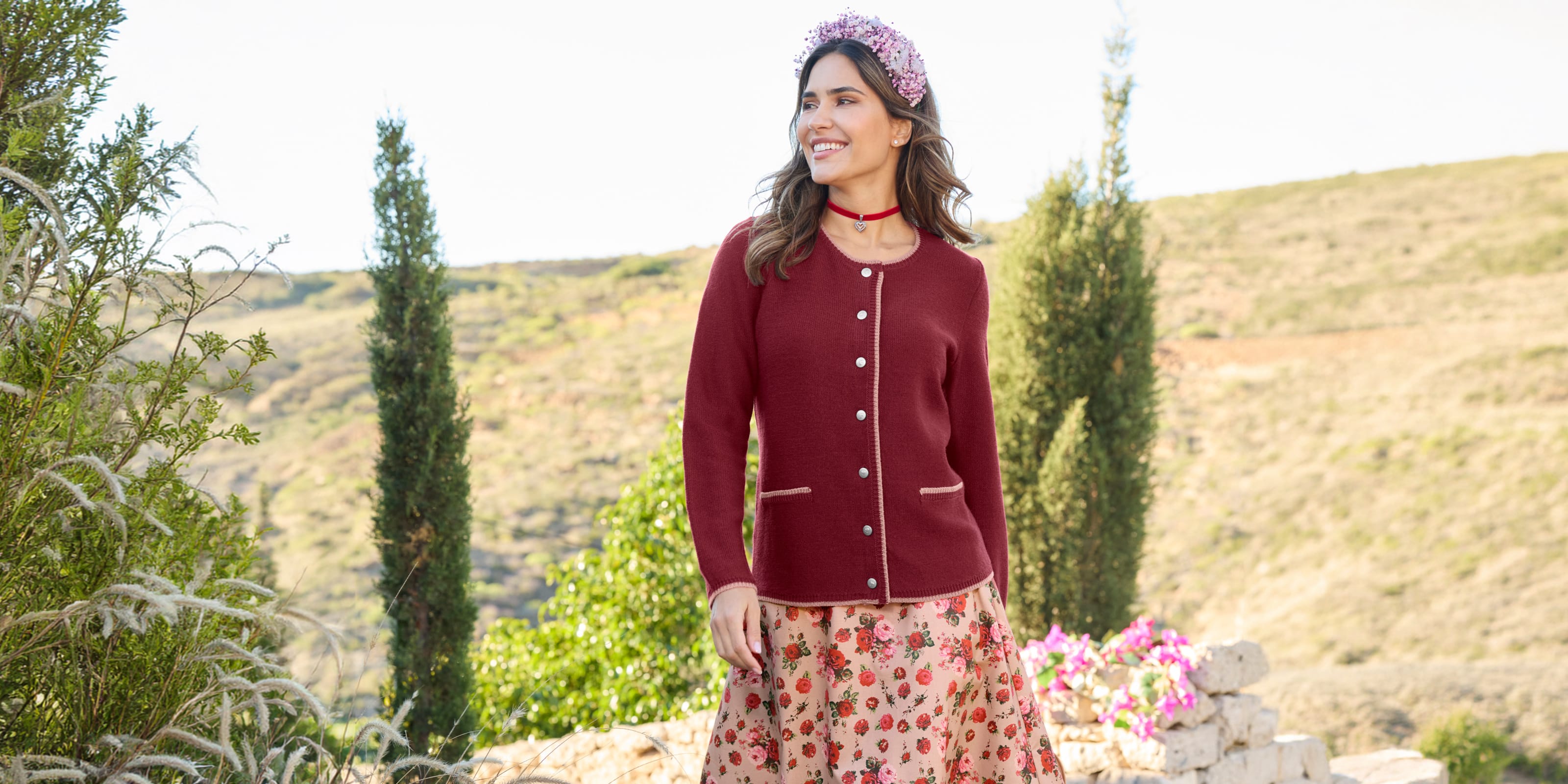 Ein Model trägt eine bordeauxrote Strickjacke und einen Rock mit Rosenmuster.