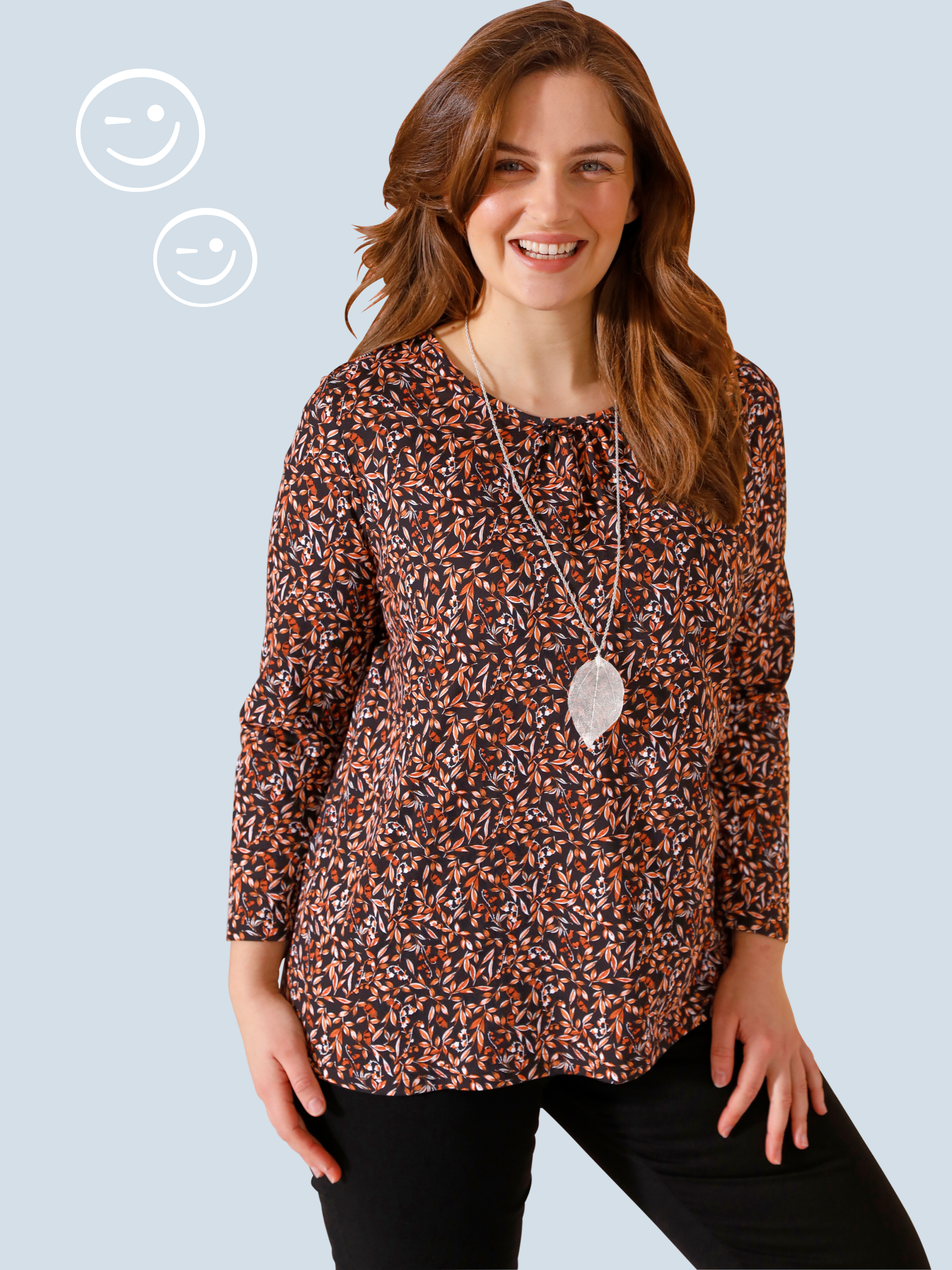 Jedna modelka má na sebe zelený top s dlhými rukávmi a kvetinovým vzorom na leme, k tomu modré džínsy, na oranžovom pozadí.