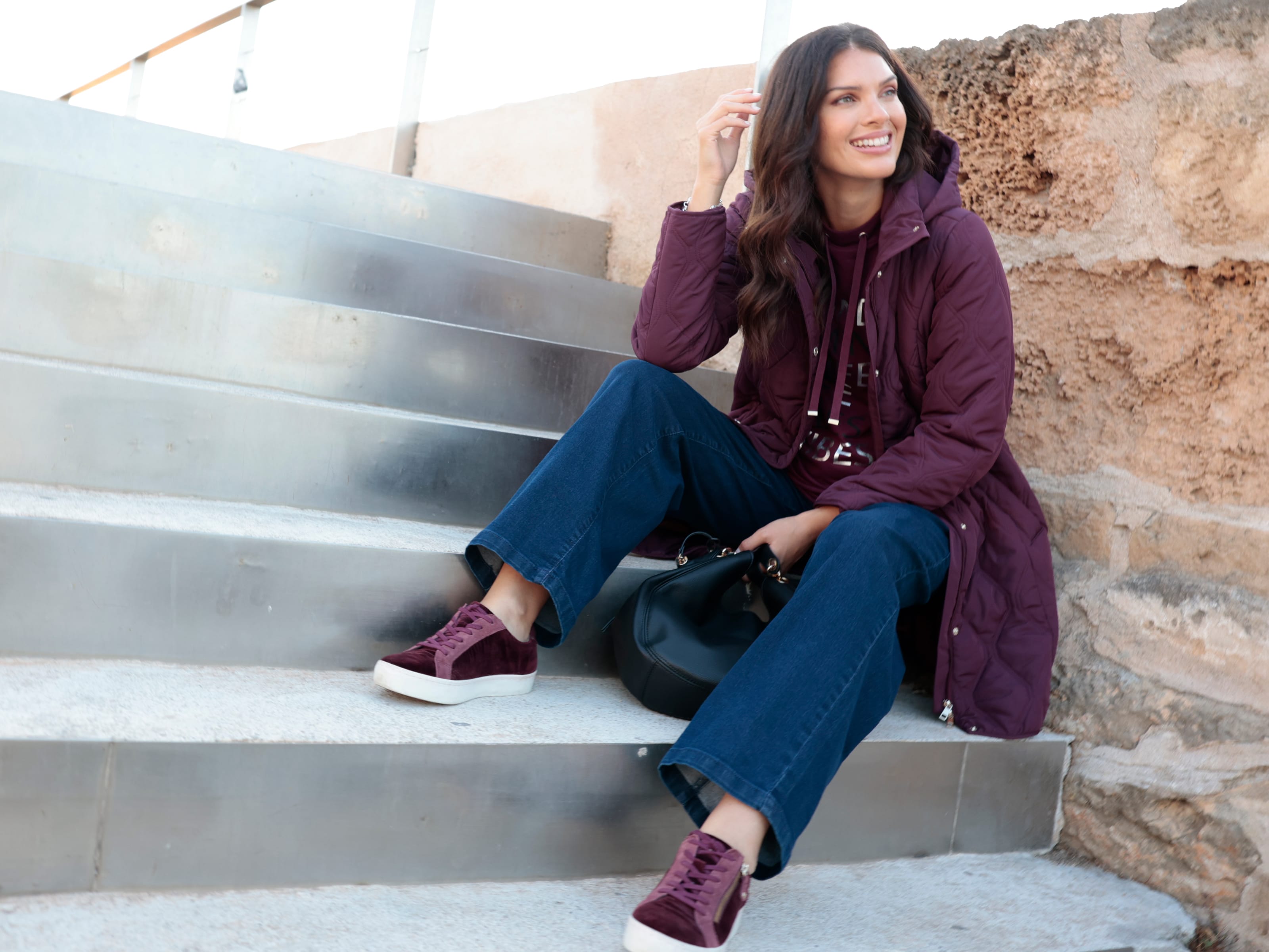 Ein Model trägt eine violette Steppjacke, Jeans und violette Turnschuhe.