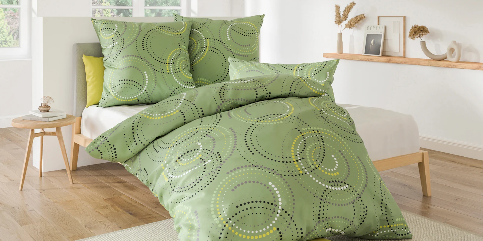 Ein Bett mit grün gemusterter Bettwäsche steht in einem hellen Schlafzimmer mit Holzboden und dekorativem Regal an der Wand.