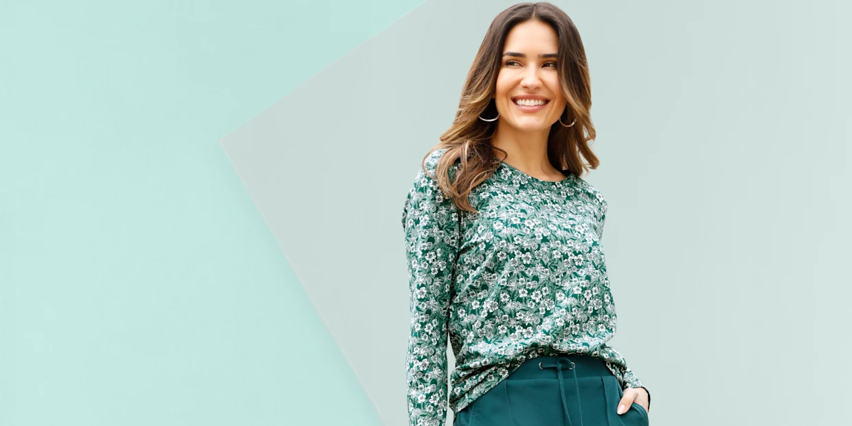 Model má na sebe zelené tričko s dlhým rukávom s bielym kvetinovým vzorom a tmavozelené nohavice so sťahovacou šnúrkou.