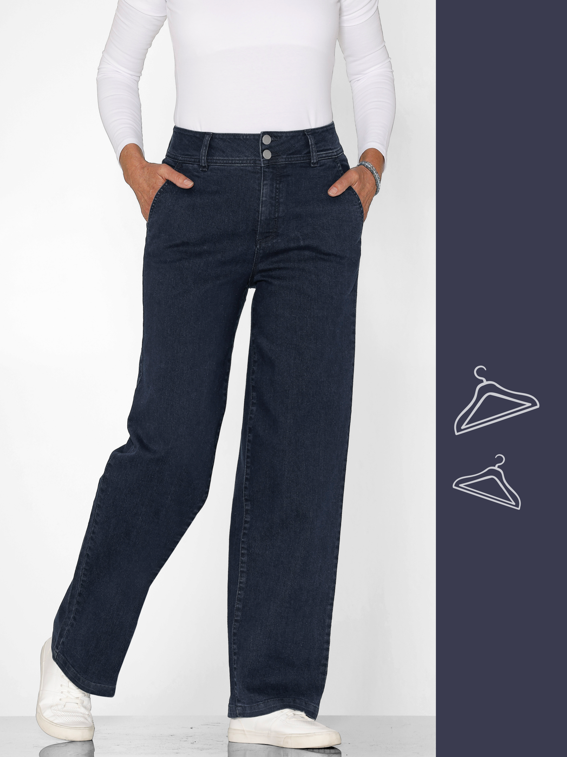 Ein Model trägt eine weiße Langarmbluse und dunkelblaue Jeans, mit den Händen in den Taschen, vor neutralem Hintergrund.