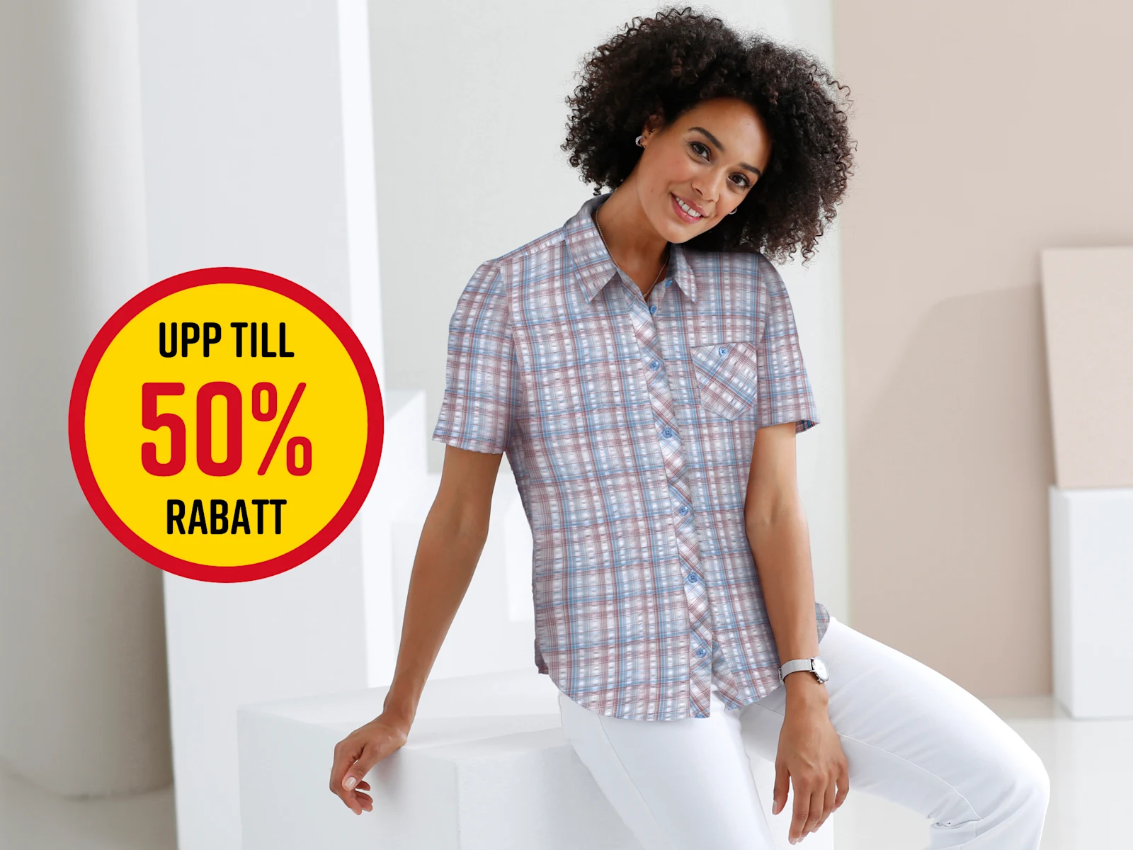 En modell med lockigt hår bär en rutig skjorta och vita byxor, sitter på en vit kub. Text i bilden: 'UPP TILL 50% RABATT'.