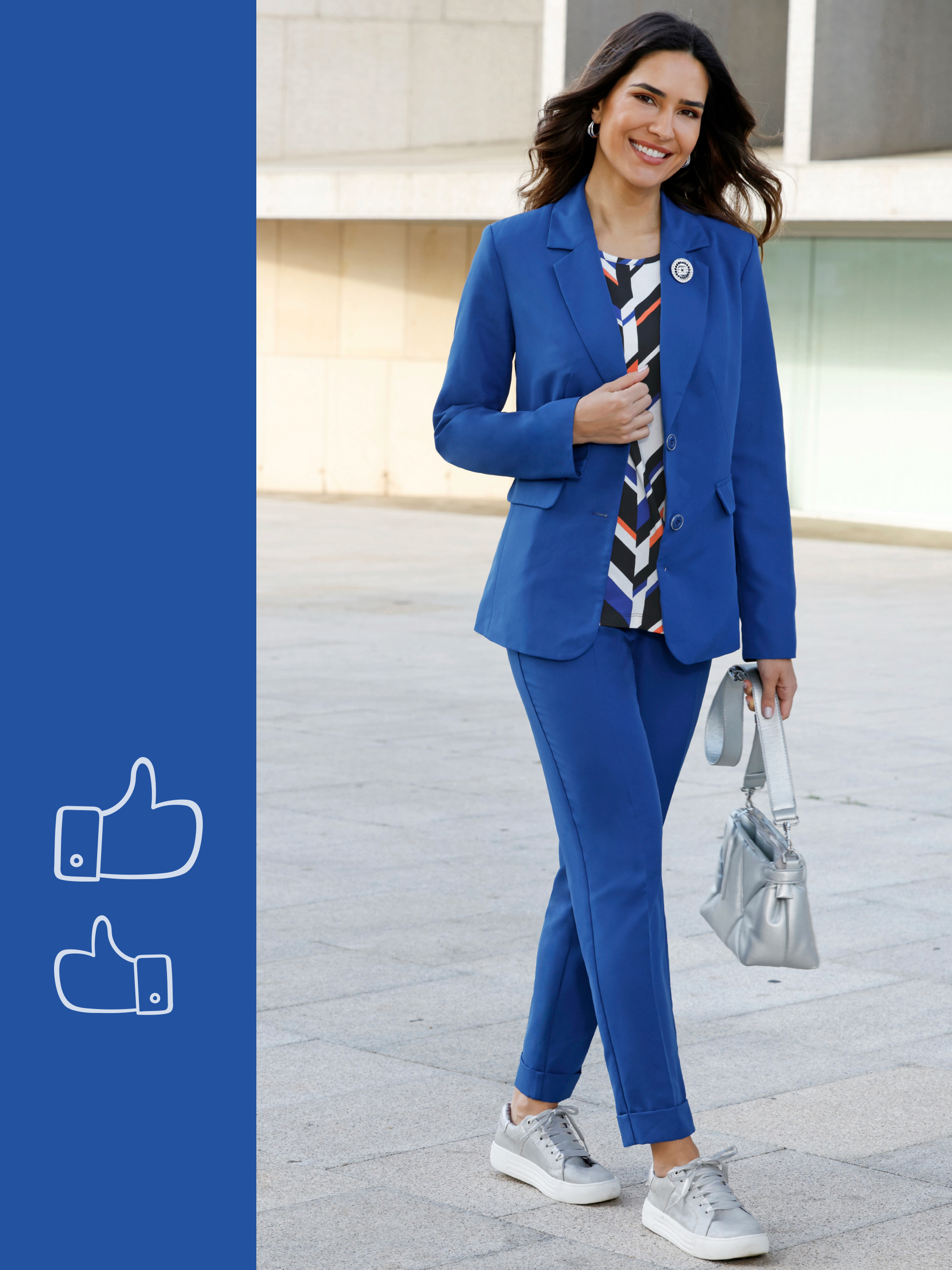 Ein Model trägt einen blauen Hosenanzug mit gemusterter Bluse, graue Sneaker und eine silberne Handtasche.