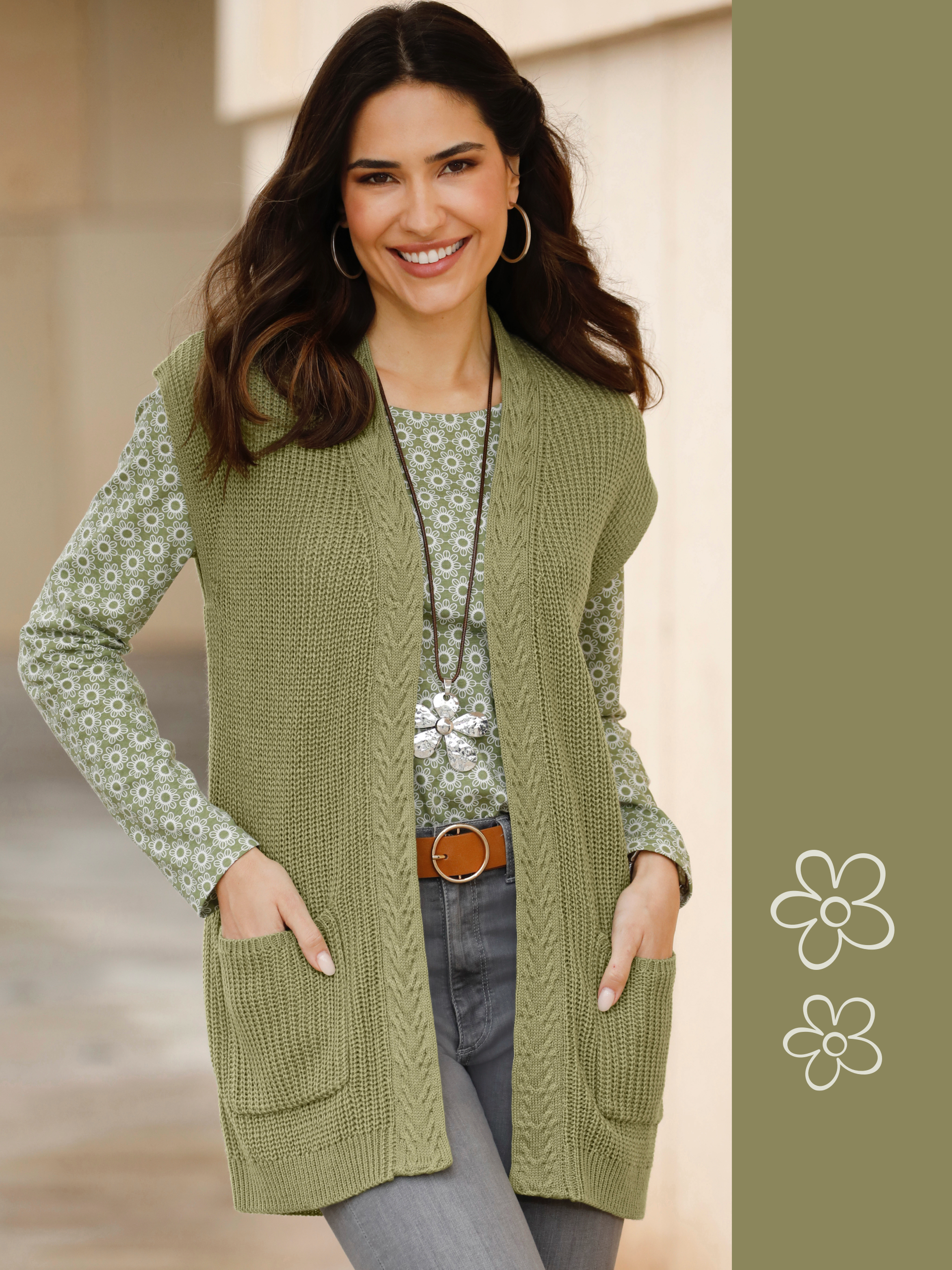 Model má na sebe zelenú pletenú vestu cez vzorované tričko s dlhým rukávom, v kombinácii so sivými džínsami a hnedým opaskom.