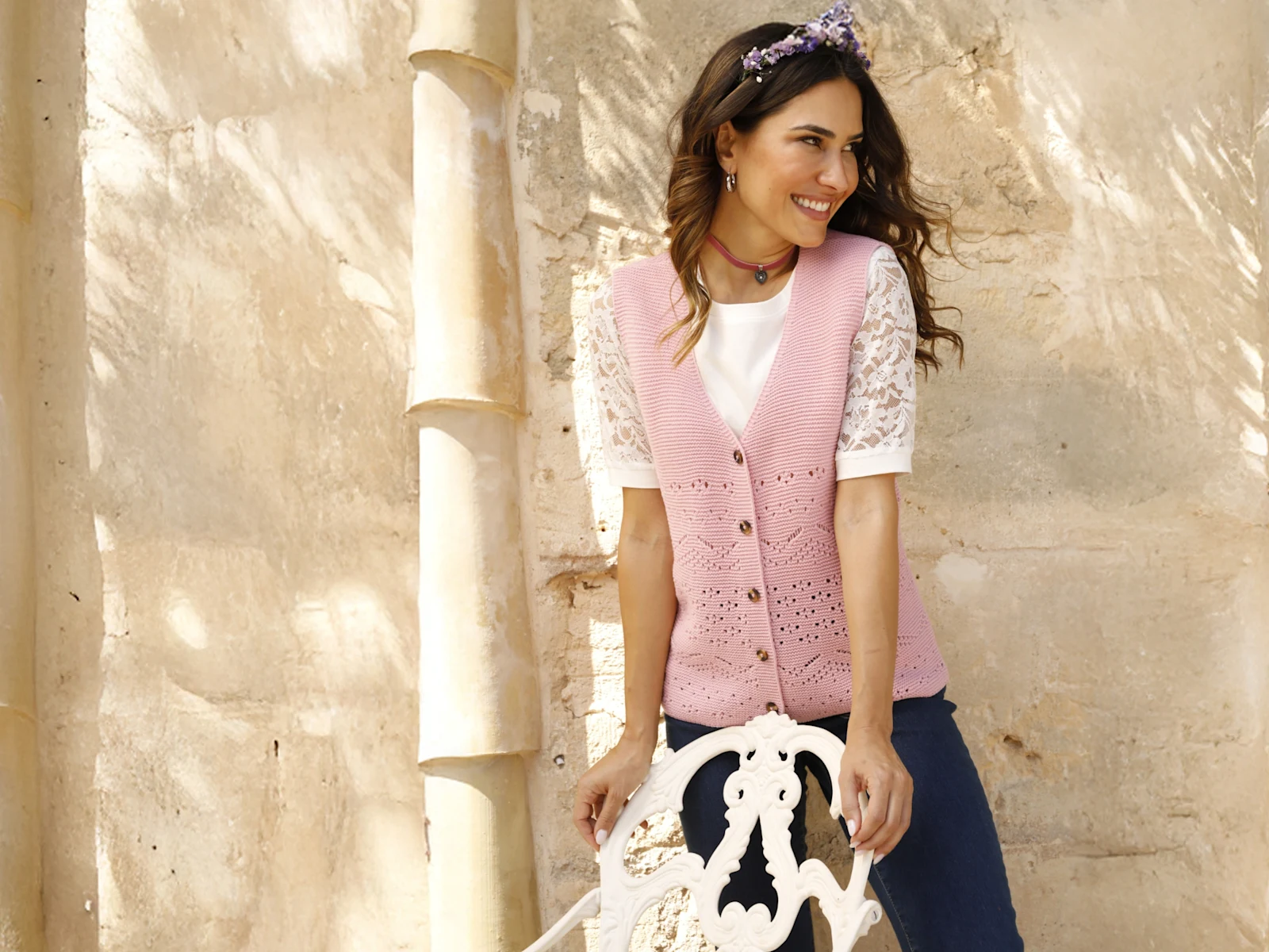 Modelka má na sebe bielu blúzku a ružovú pletenú vestu pred svetlým pozadím.