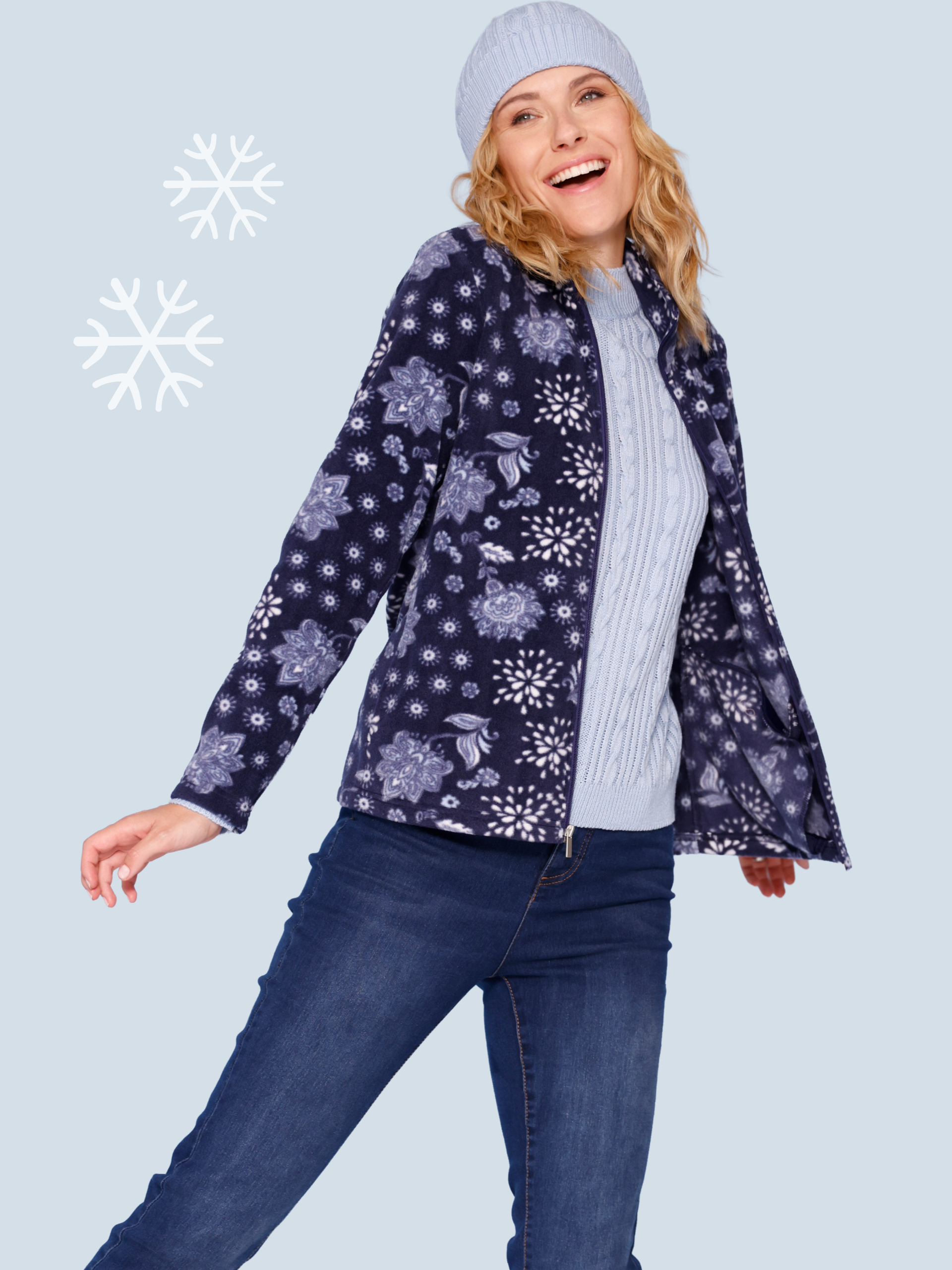 Ein Model trägt eine blaue Winterjacke mit floralem Muster, eine Mütze und Jeans.