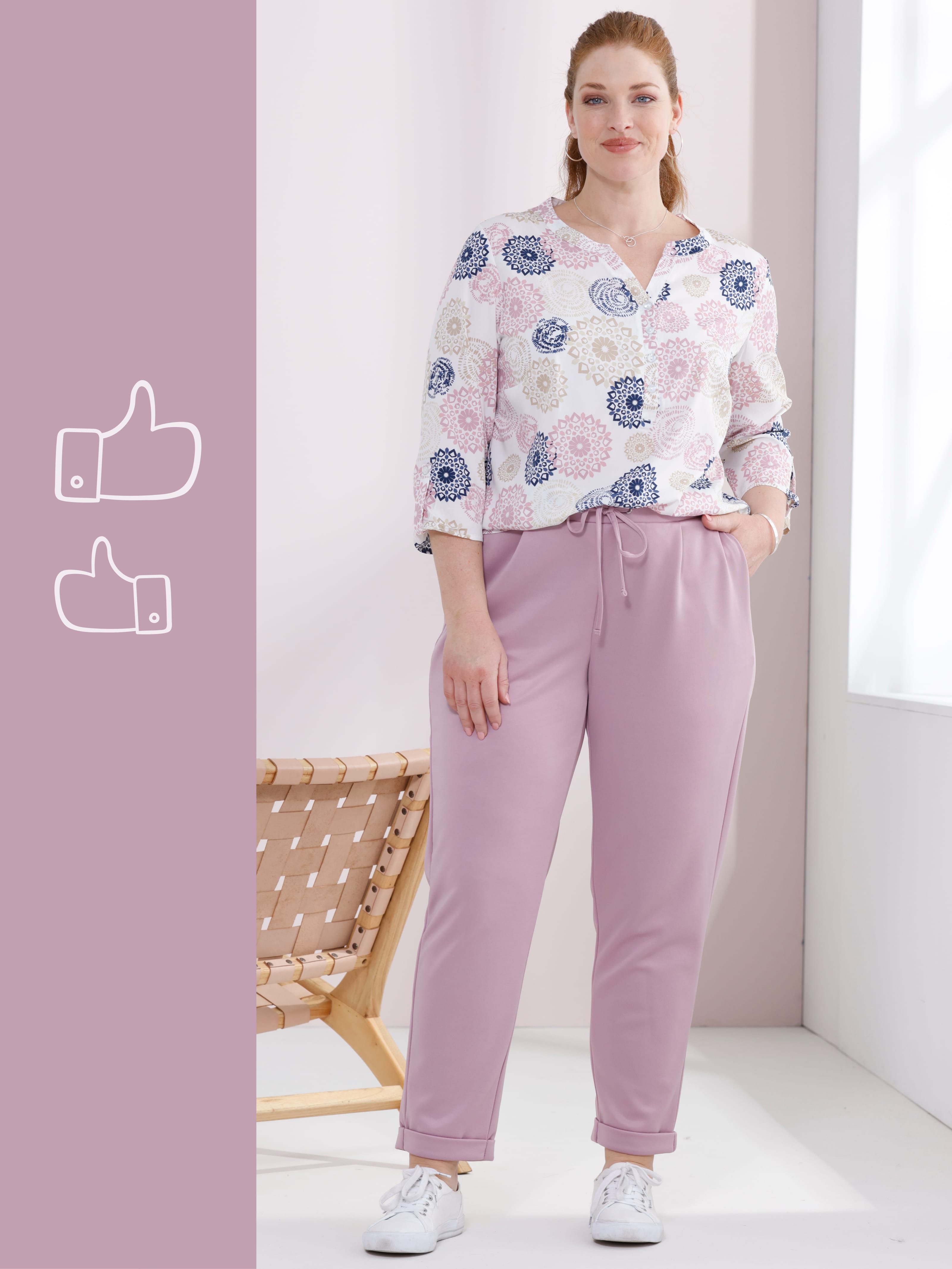 Ein Model trägt eine weiße Bluse mit Muster und helle, lockere Hose mit Kordelzug.