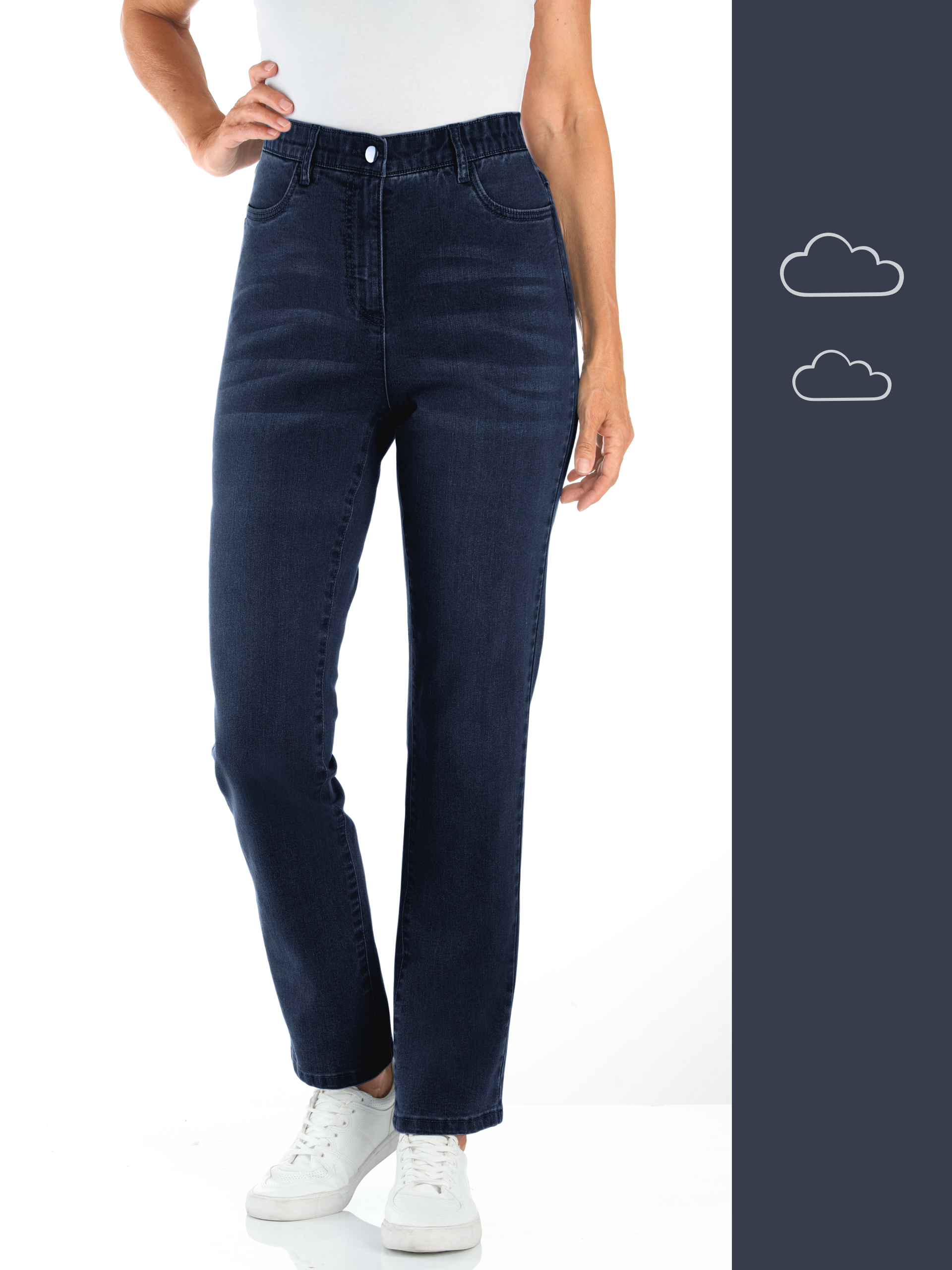 Ein Model trägt dunkelblaue Jeans mit hohem Bund und weiße Sneaker, steht vor weißem Hintergrund.