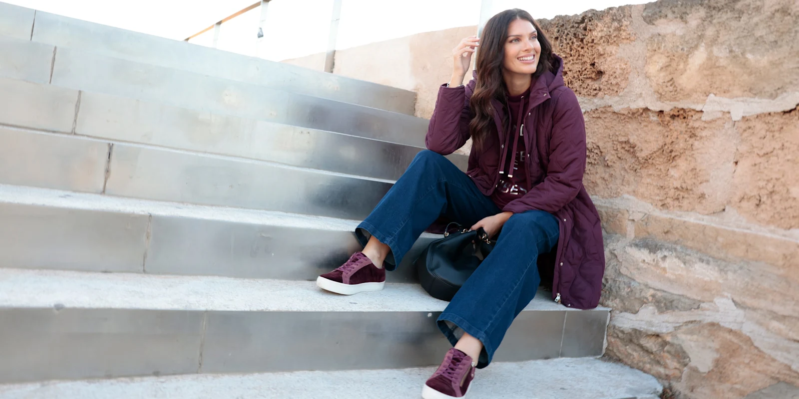 Ein Model trägt eine violette Steppjacke, Jeans und violette Turnschuhe.