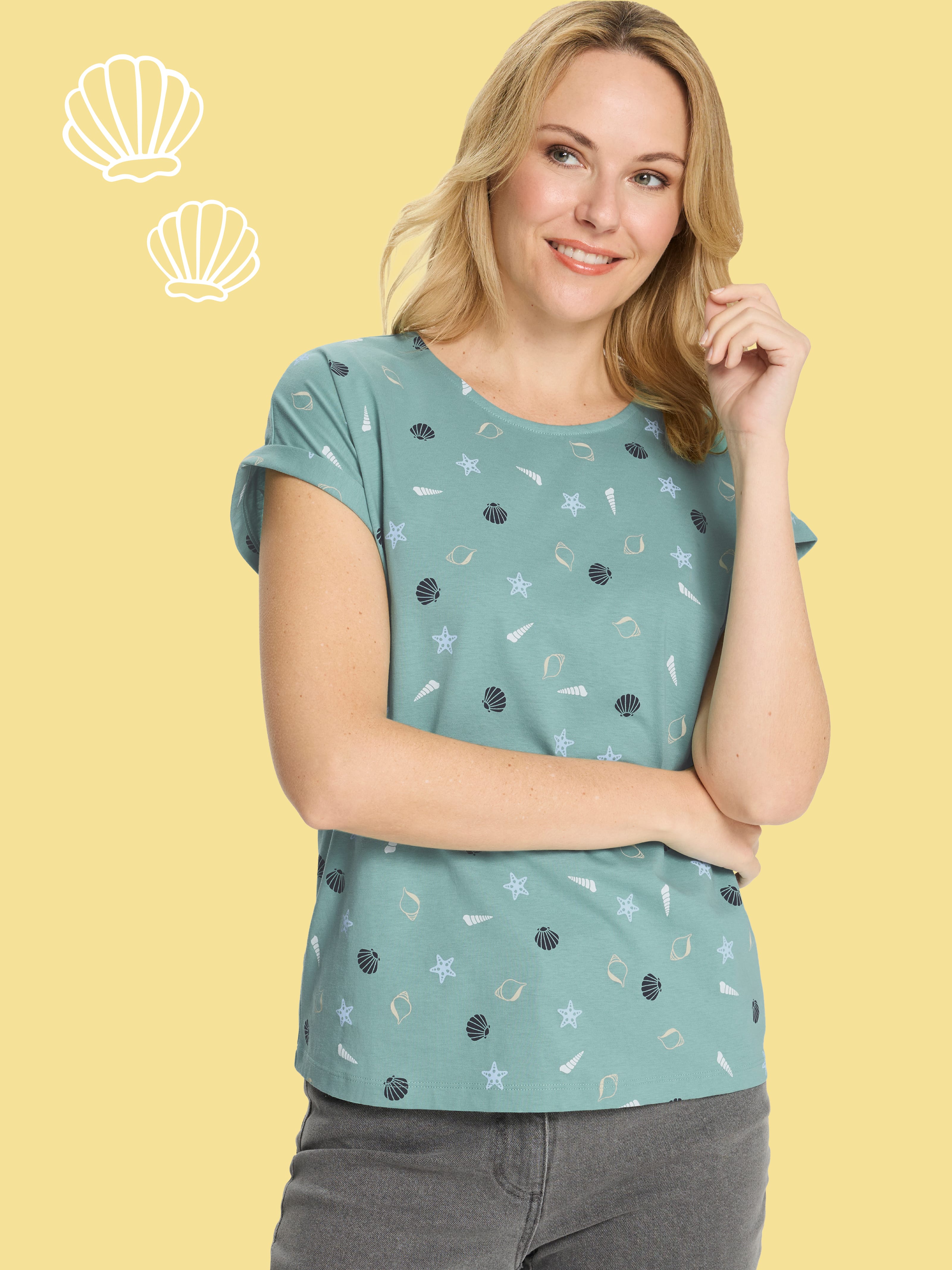 En modell bär en grön t-shirt med ett marint mönster av snäckor och sjöstjärnor.