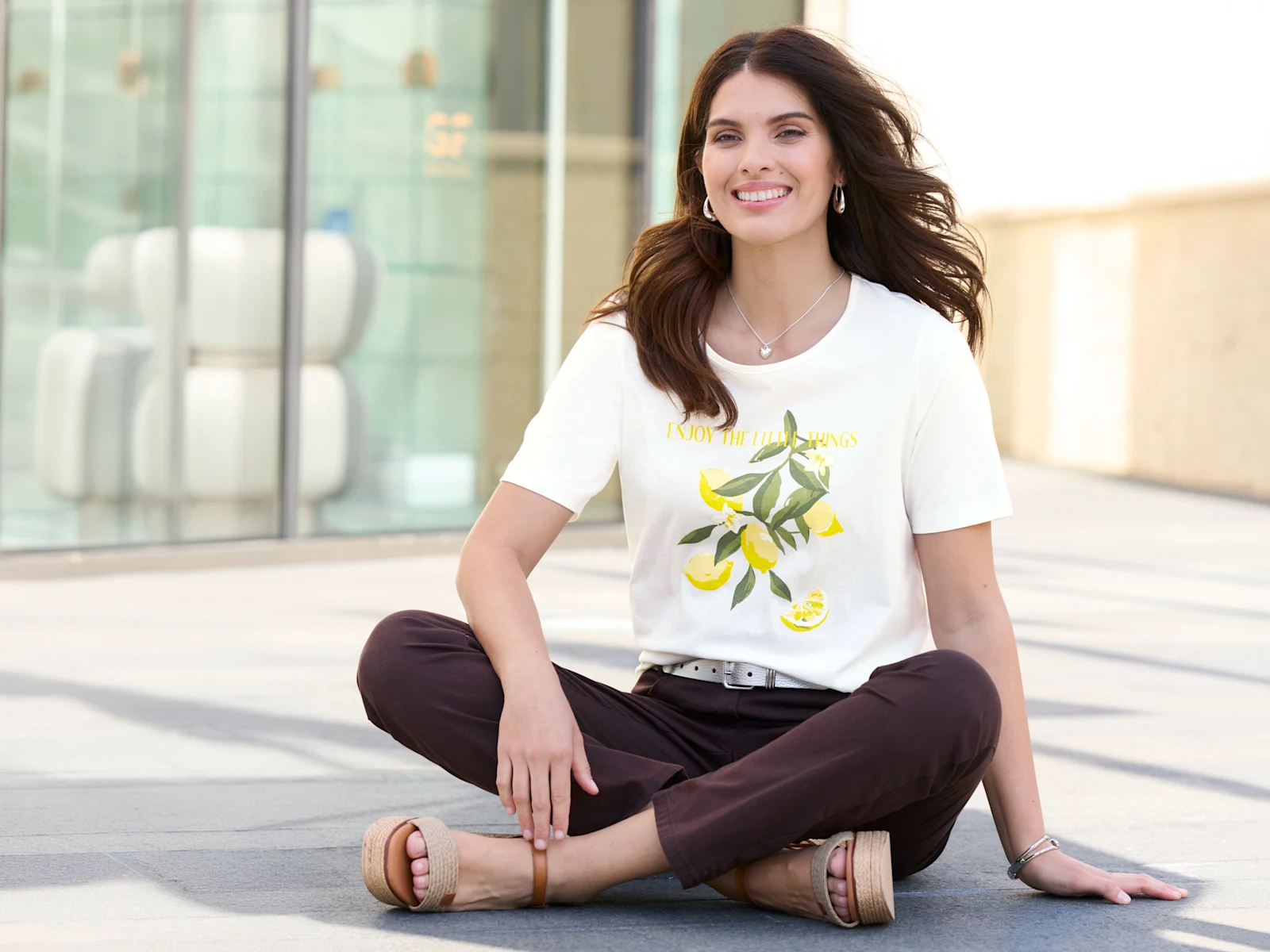 Ein Model mit langen dunklen Haaren trägt ein weisses T-Shirt mit Zitronenmotiv und eine Hose.