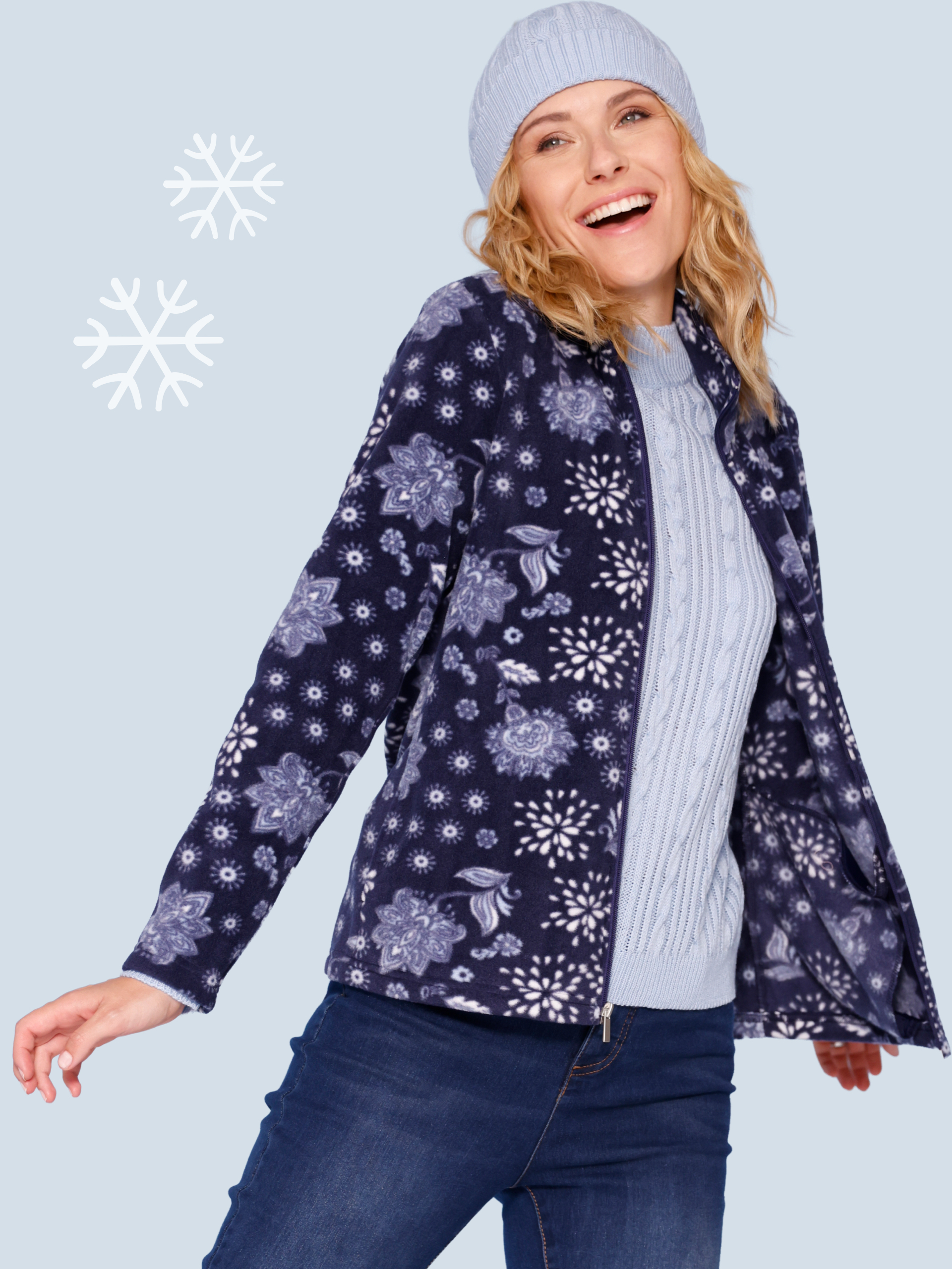 Model má na sebe modrú zimnú bundu s kvetinovým vzorom, čiapku a rifle.