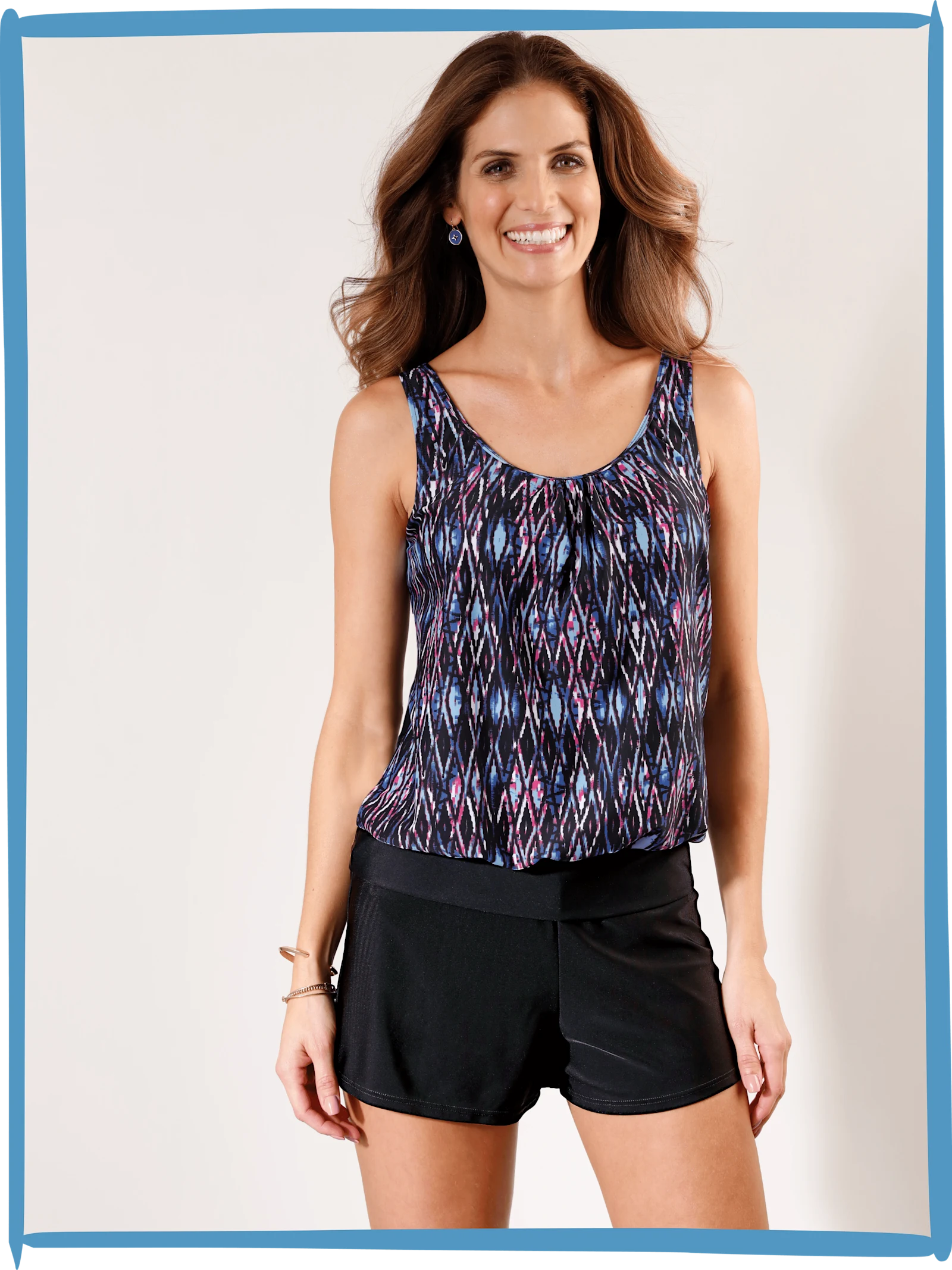 Ein Model trägt einen gemusterten Tankini-Oberteil und schwarze Shorts.