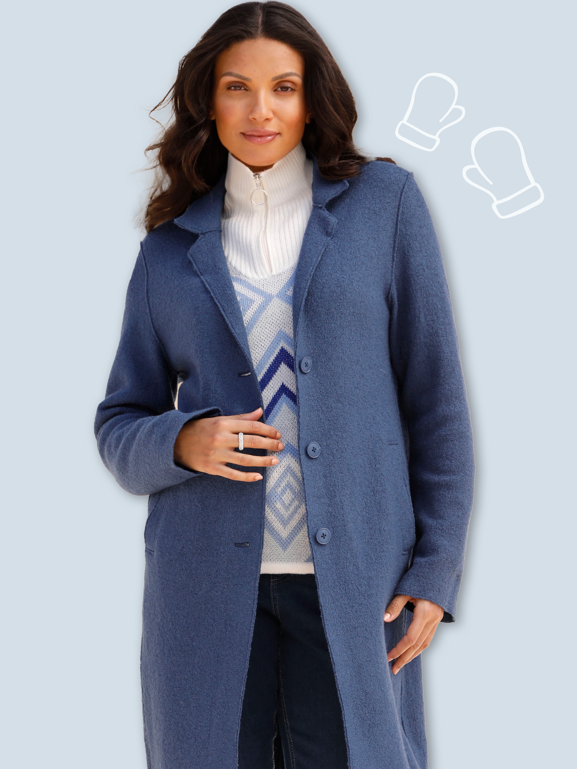 Een model met donker haar draagt een lange blauwe jas, een wit vest en een jeans.