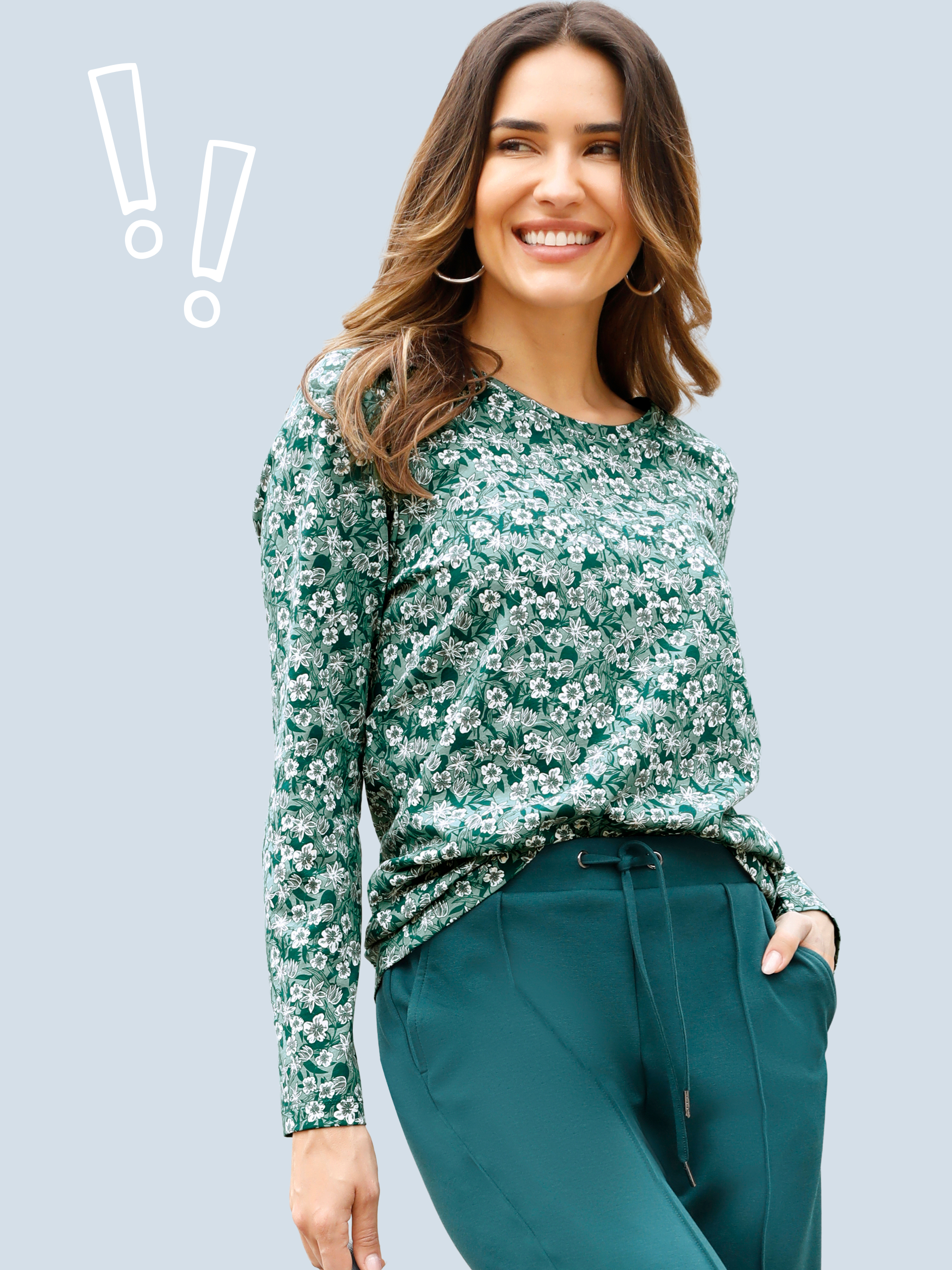 Model má na sobě zelené tričko s dlouhým rukávem s bílým květinovým vzorem a tmavě zelené kalhoty se šňůrkou.