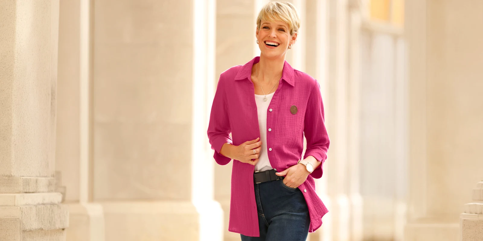 Model má na sobě růžovou dlouhou košili přes bílé tričko a modré džíny.