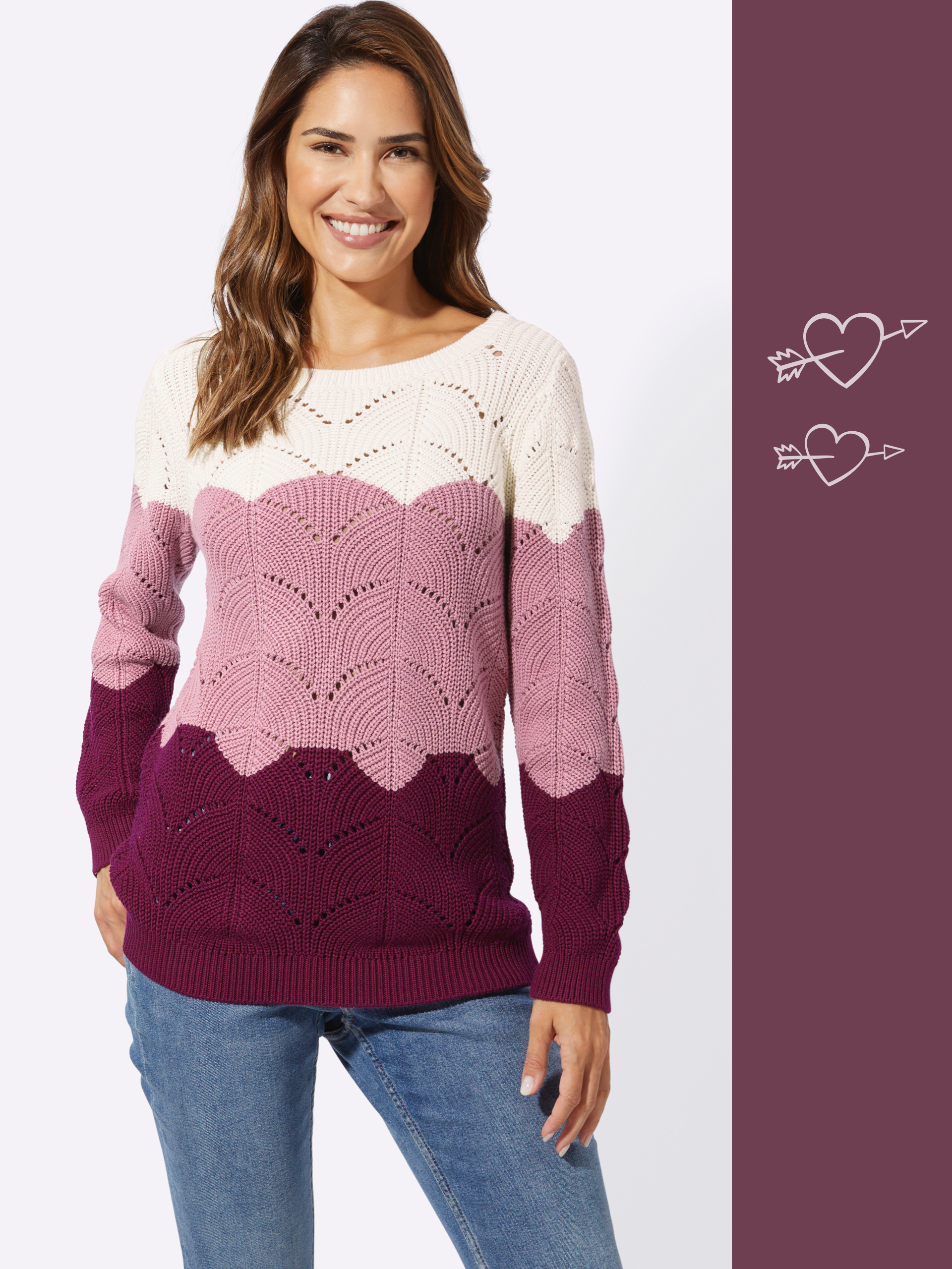 Model má na sebe pletený sveter s farebným prechodom od bielej cez ružovú po tmavočervenú, v kombinácii s modrými džínsami.