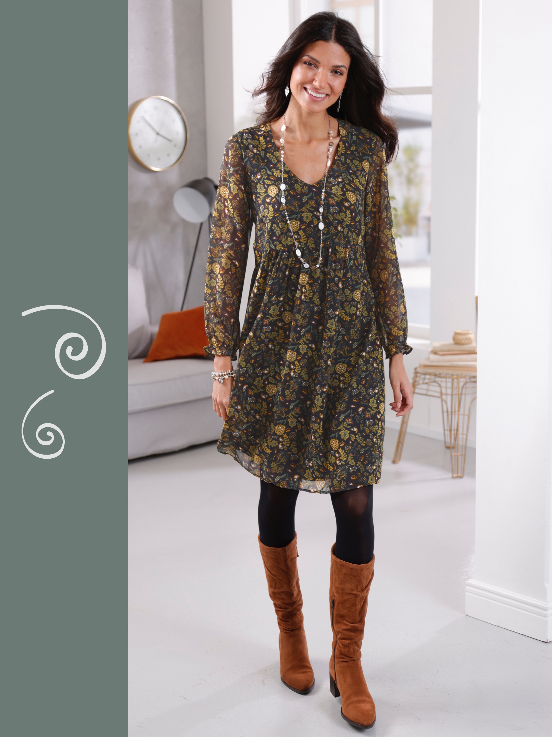 Ein Model präsentiert ein gemustertes, schwarzes Kleid mit langen Ärmeln, schwarzer Strumpfhose und braunen Stiefeln. Sie trägt eine lange Kette und Ohrringe.