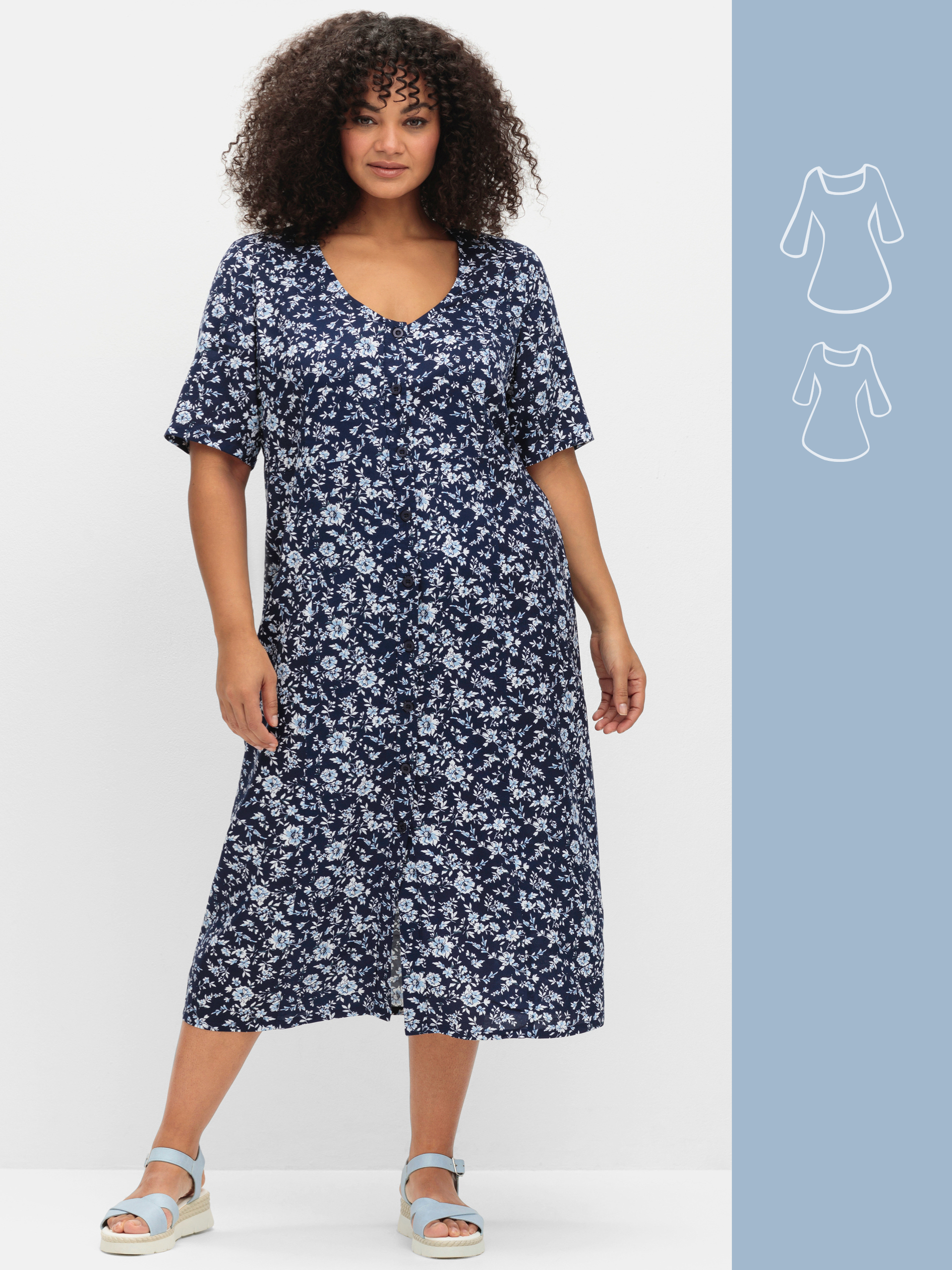 Ein Model trägt ein dunkelblaues, knielanges Kleid mit weißem Blumenmuster und kurzen Ärmeln.