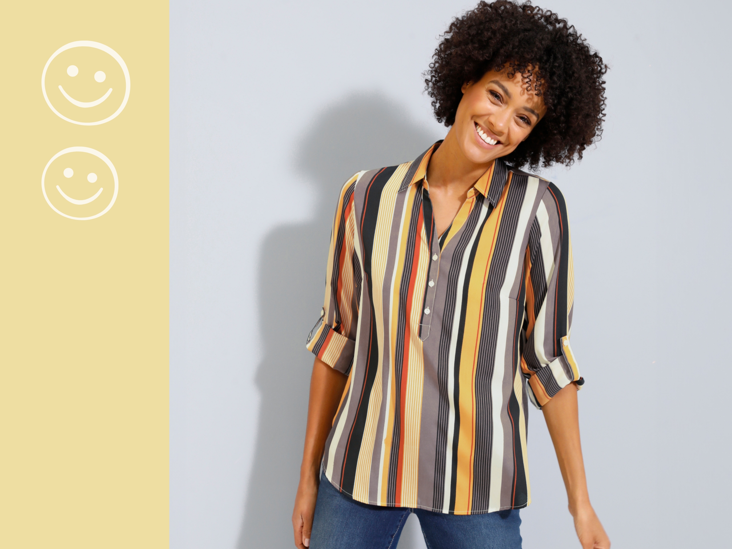 Gestreifte Bluse in Gelb-, Orange- und Schwarztönen, kombiniert mit einer Jeans vor hellem Hintergrund.