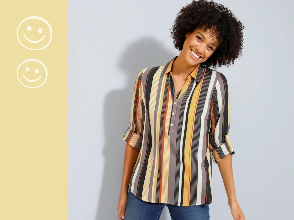 Gestreifte Bluse in Gelb-, Orange- und Schwarztönen, kombiniert mit einer Jeans vor hellem Hintergrund.