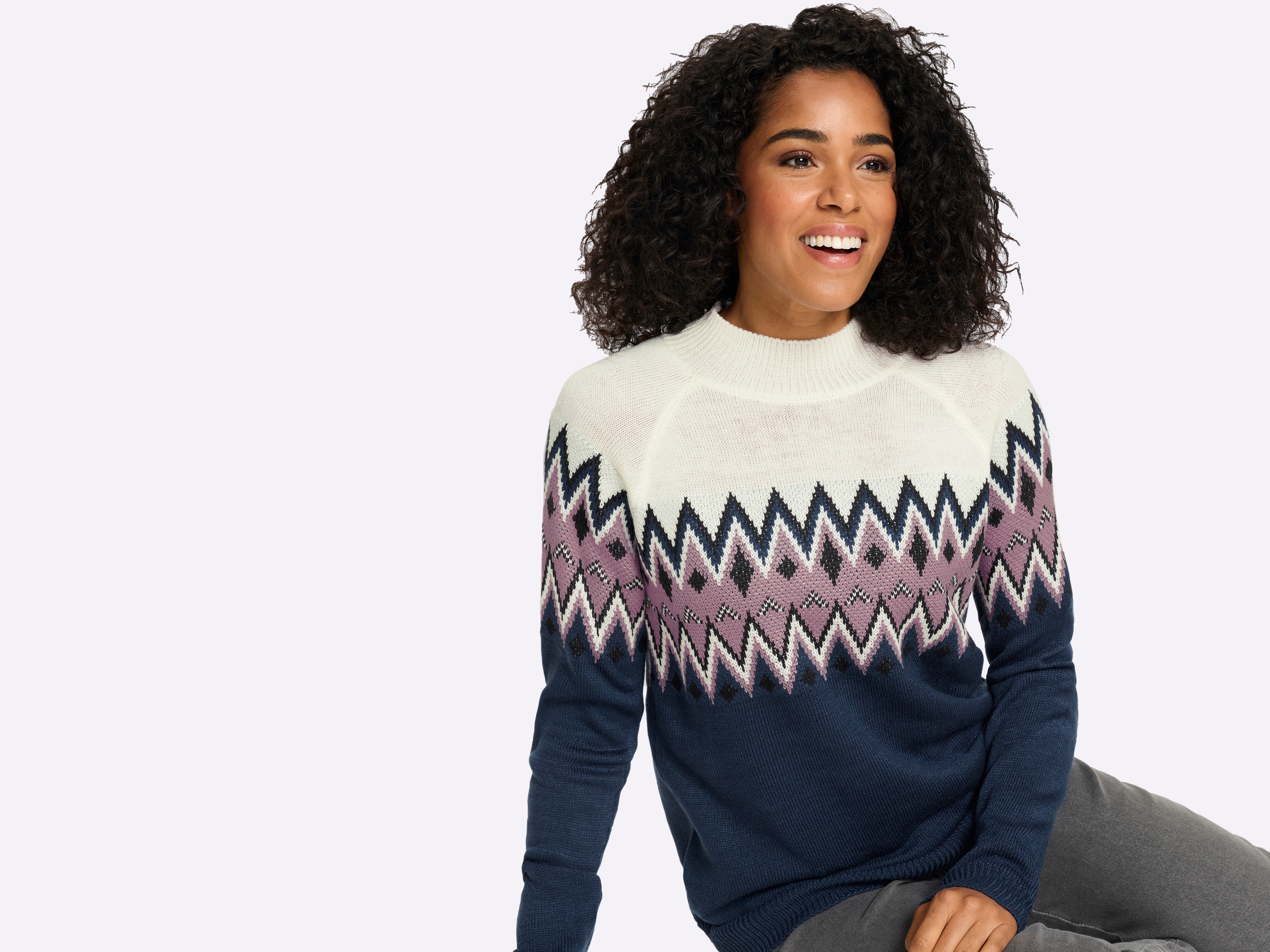 Ein Model trägt einen Strickpullover mit Rundhalsausschnitt und geometrischem Zickzackmuster in Blau, Weiß und Rosa.