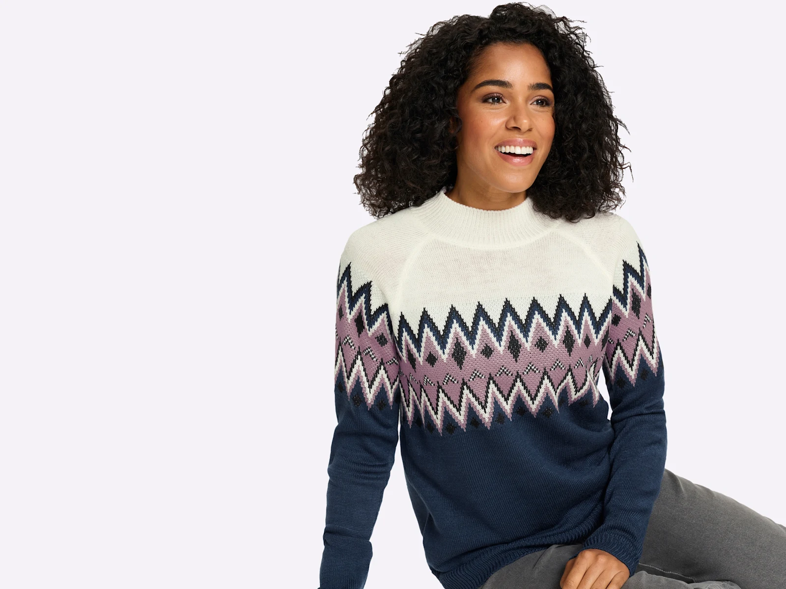 Ein Model trägt einen Strickpullover mit Rundhalsausschnitt und geometrischem Zickzackmuster in Blau, Weiß und Rosa.