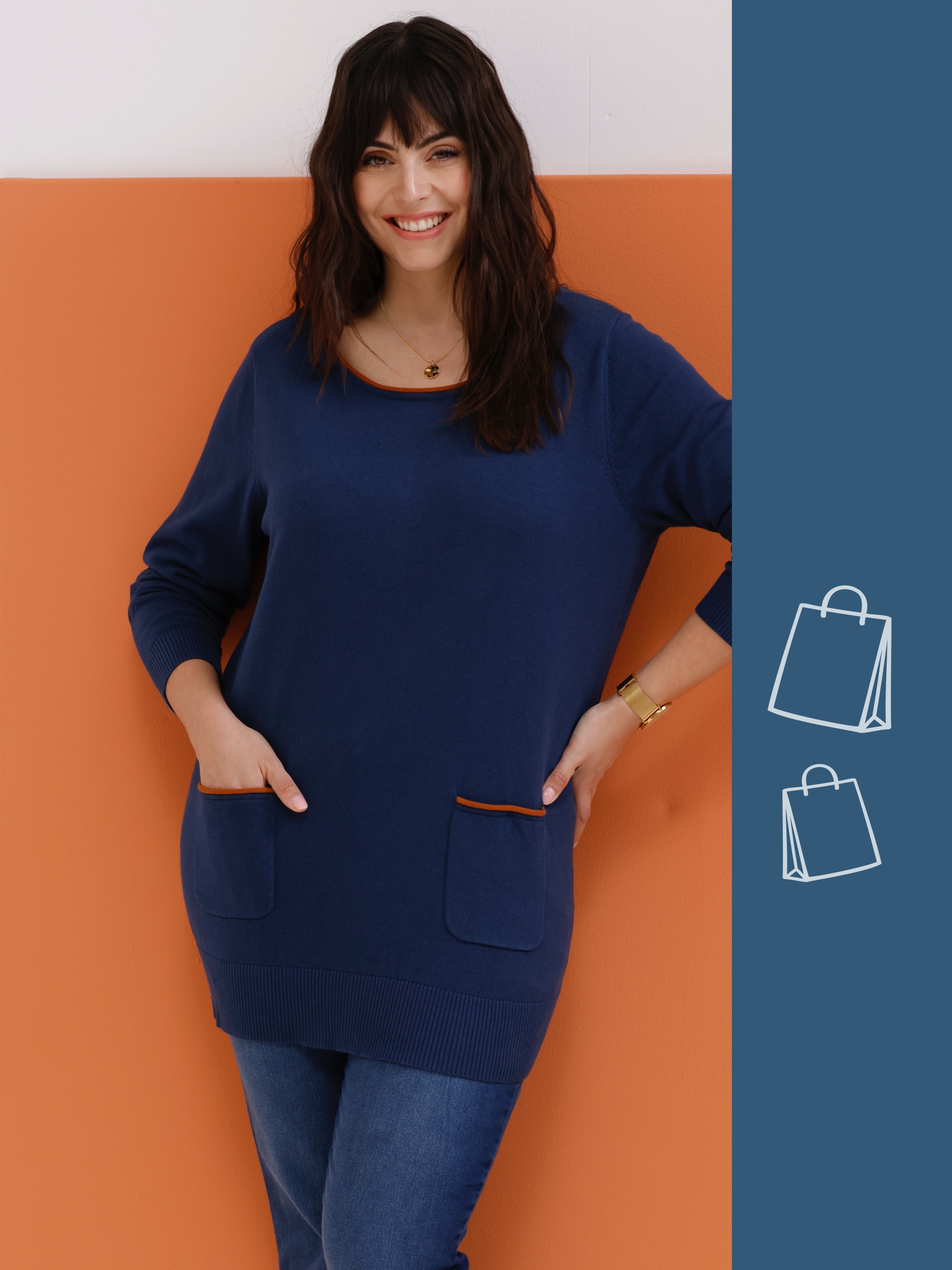 Ein Model steht vor einem orangefarbenen Hintergrund in einem blauen Pullover mit Taschen und Jeans.