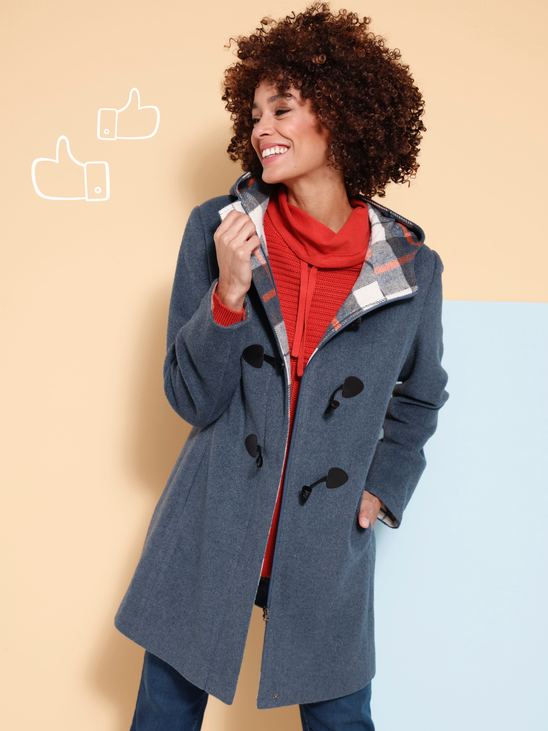 Ein Model trägt einen grauen Mantel mit schwarzen Knebelknöpfen, darunter ein roter Pullover mit Rollkragen, vor einer zweifarbigen Wand.