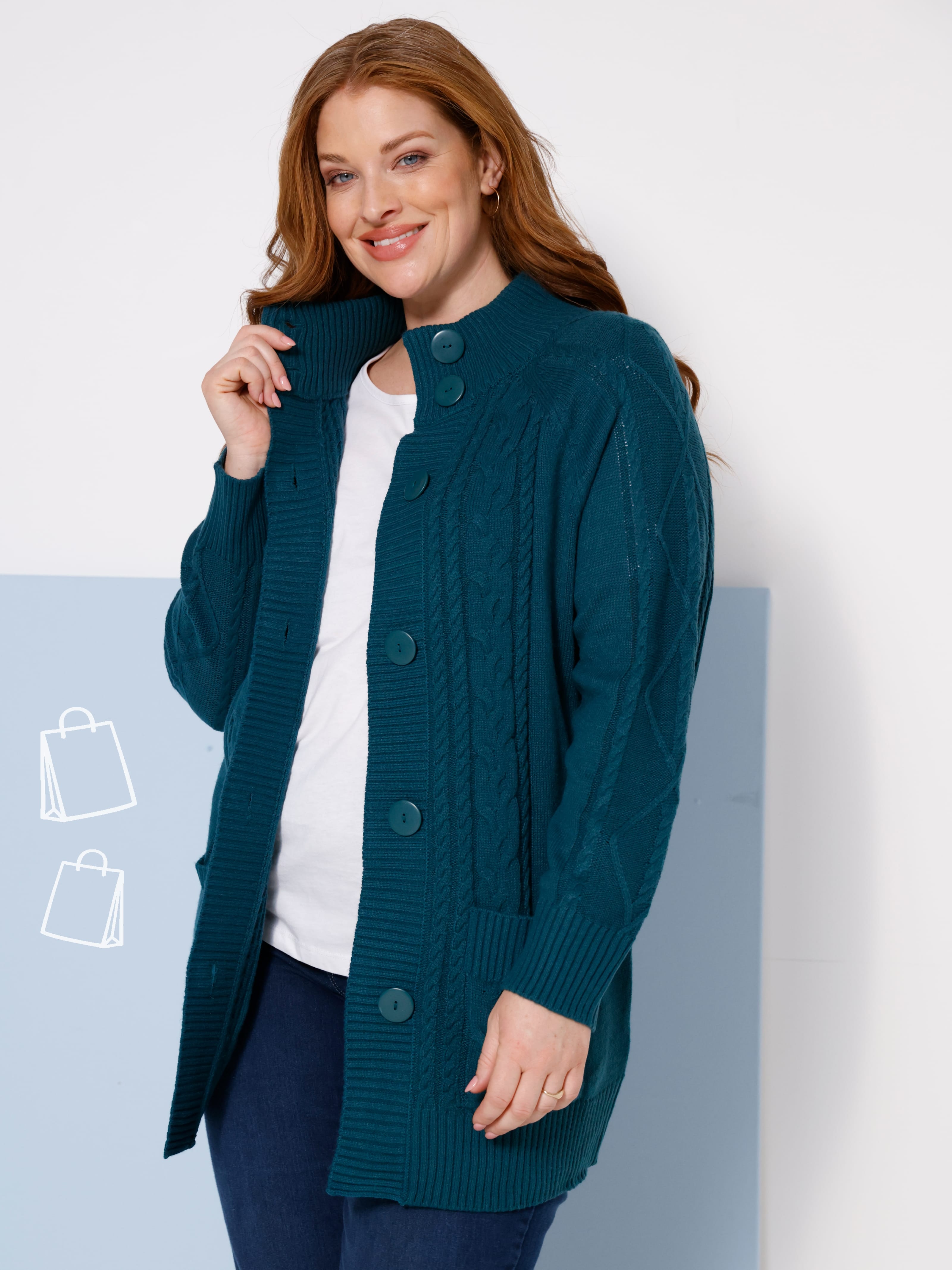 Ein Model trägt eine dunkelblaue Strickjacke über weißem Oberteil und dunkler Hose.