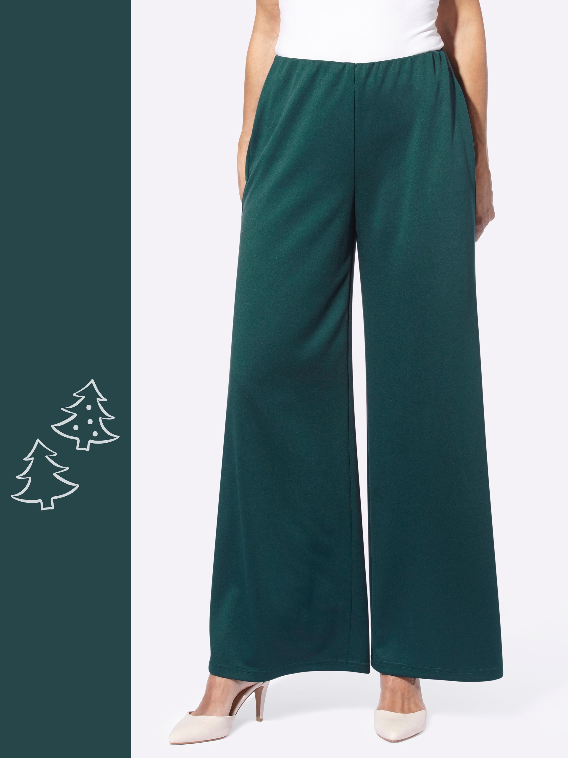 Ein Model trägt weite, dunkelgrüne Hosen mit elastischem Bund und weiße Pumps, Hände in den Taschen.