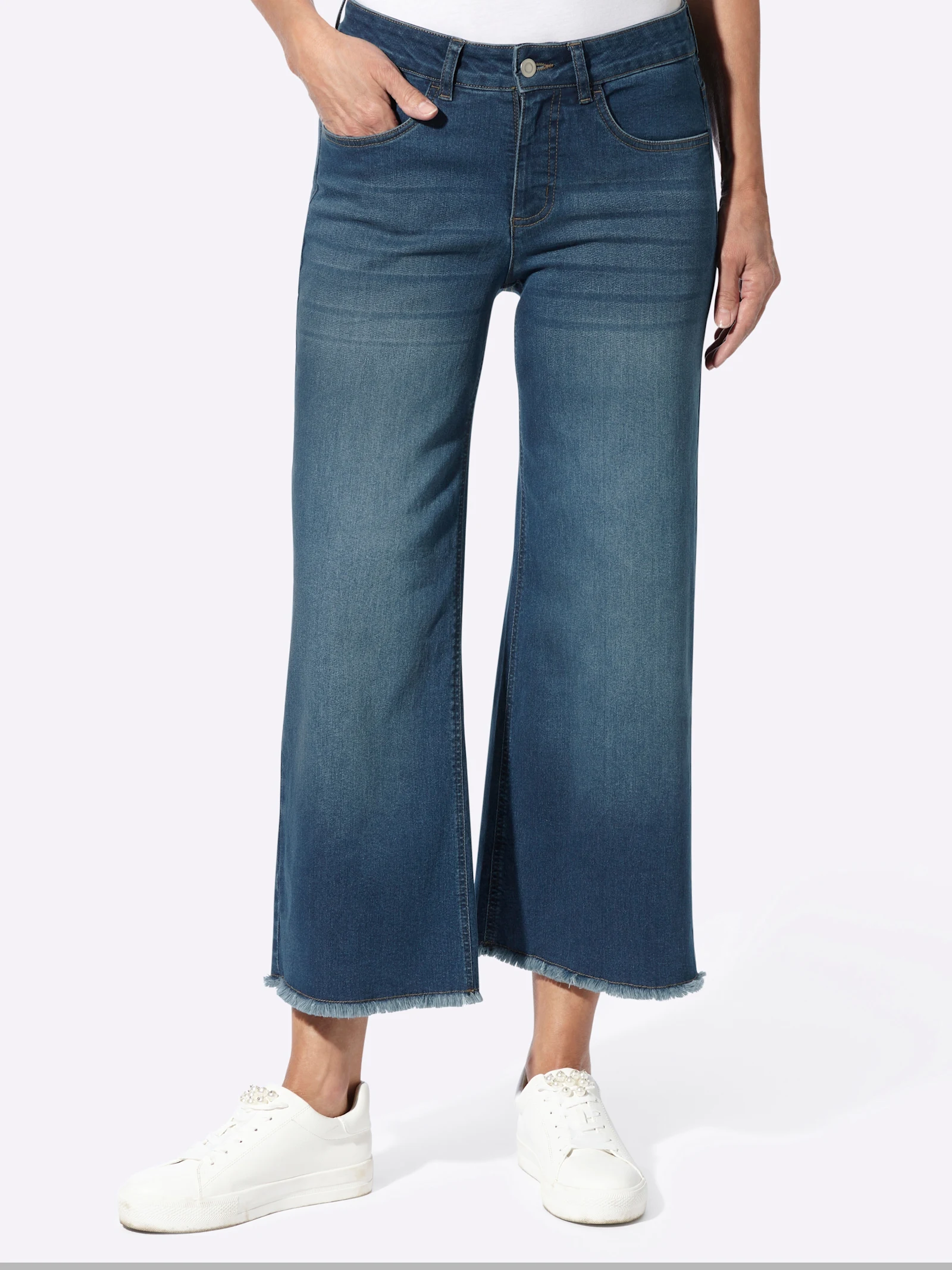 Ein Model trägt eine dunkelblaue Jeans mit weitem, verkürztem Bein und weißen Sneakern.