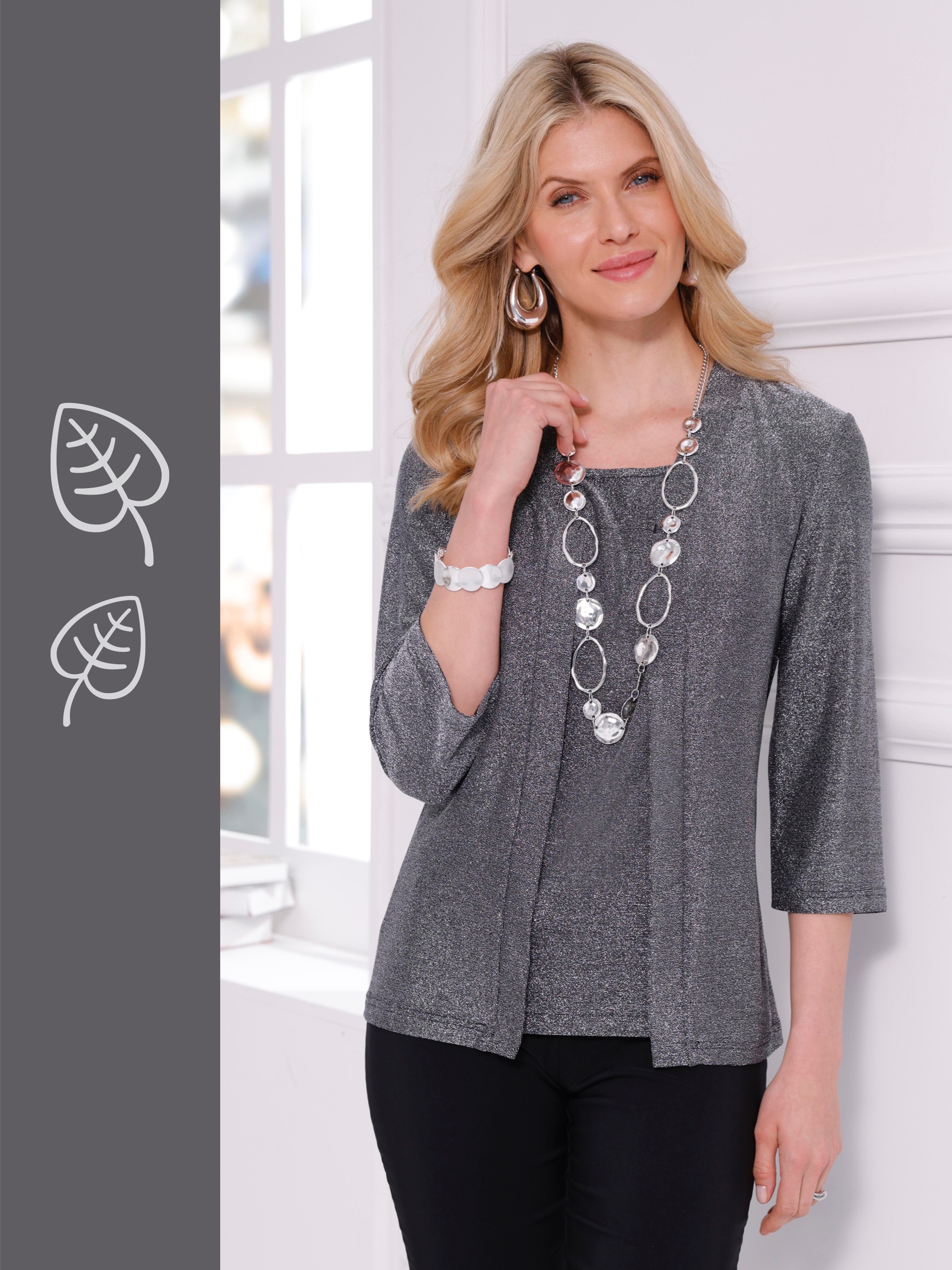 Ein Model mit langen, blonden Haaren trägt eine graue, dreiviertelärmelige Strickjacke über einem passenden Top und eine lange, silberne Halskette.