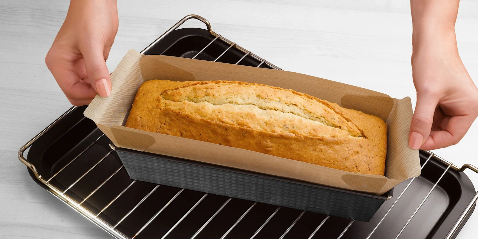 Zwei Hände greifen nach einer Backform mit frisch gebackenem Kuchen.