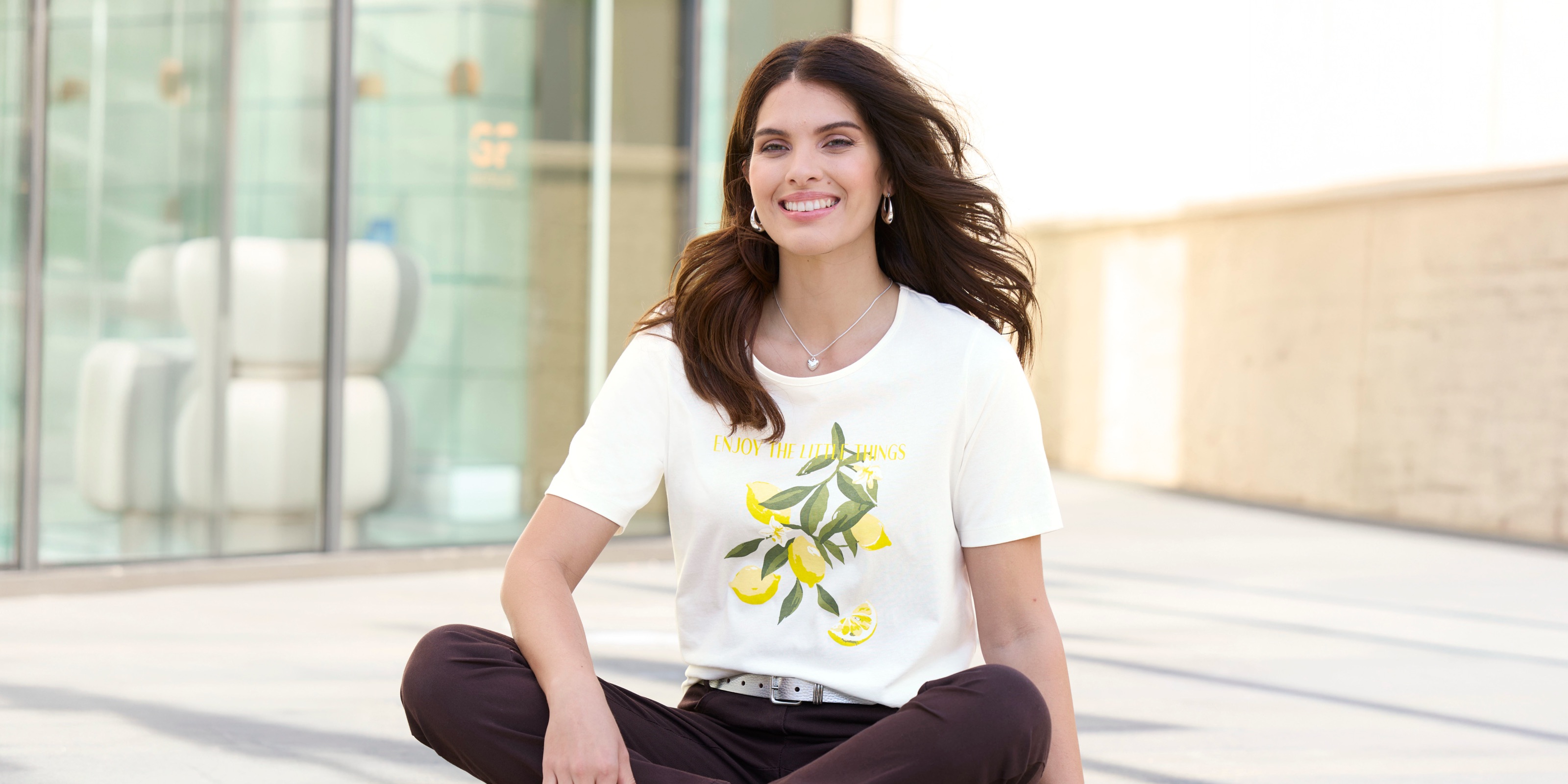 Ein Model mit langen dunklen Haaren trägt ein weisses T-Shirt mit Zitronenmotiv und eine Hose.